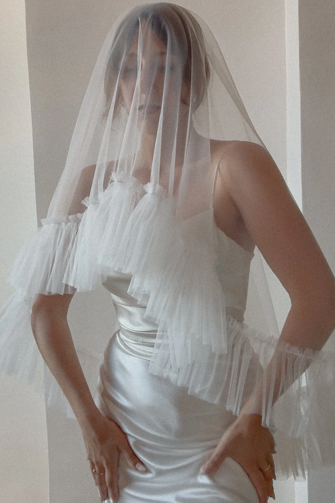 A bride with a soft off-white tulle wedding veil with a ruffled edge