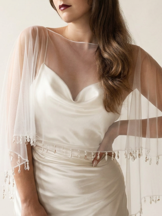 A bride wearing a tulle bridal shawl with pearl beads and glass droplets along the edge