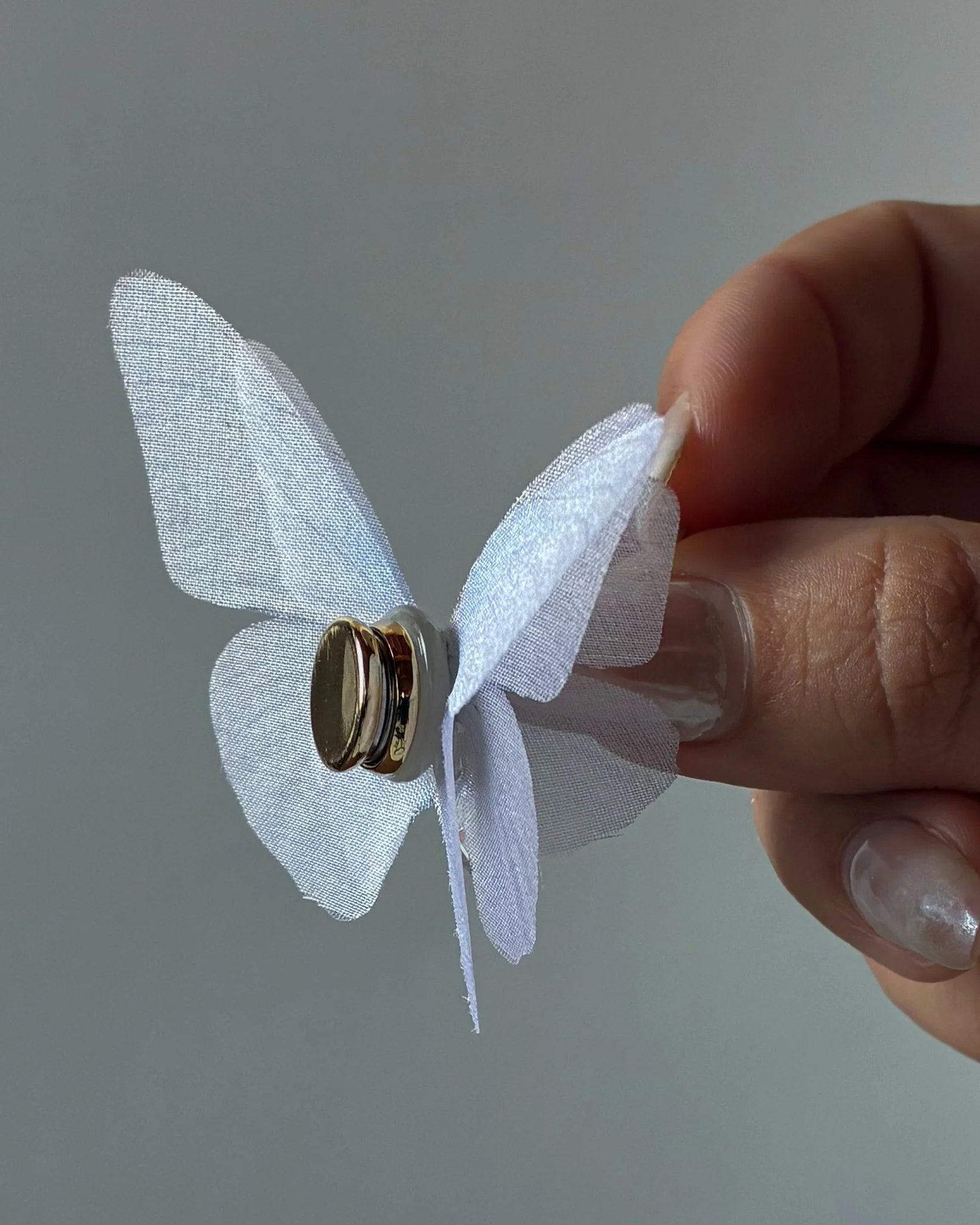 Three-layer white silk butterfly bridal accessory with magnetic backing and a shimmering glass droplet
