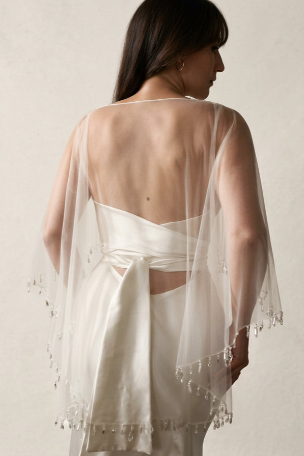 The back of a bride wearing a tulle bridal cape with crystal droplets along the edge
