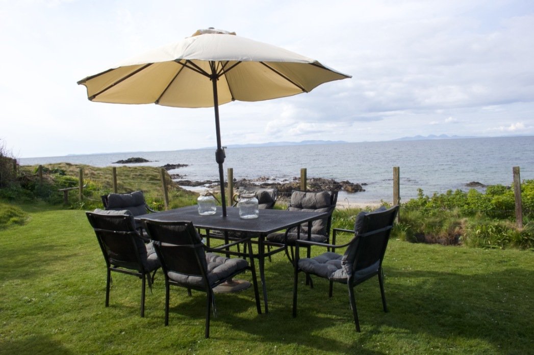 Garden table and chairs with parasol in garden overlooking sea.