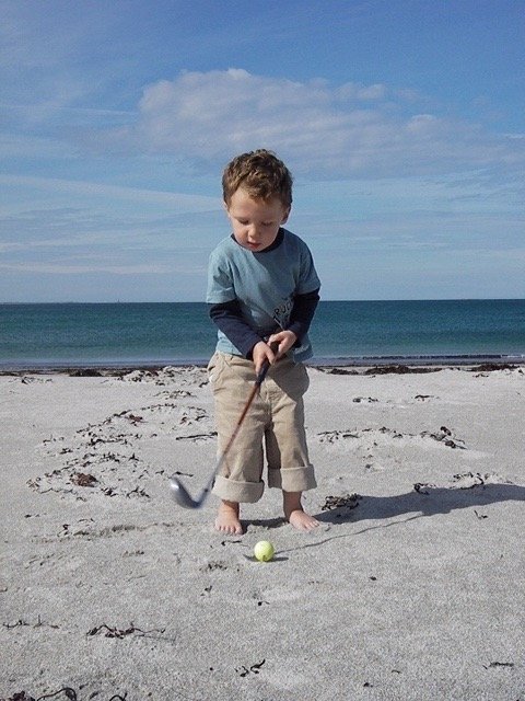 Little boy playing golf on the beach.