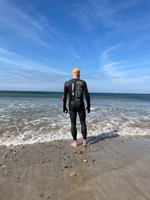 Man in black wetsuit standing at the edge of the sea.