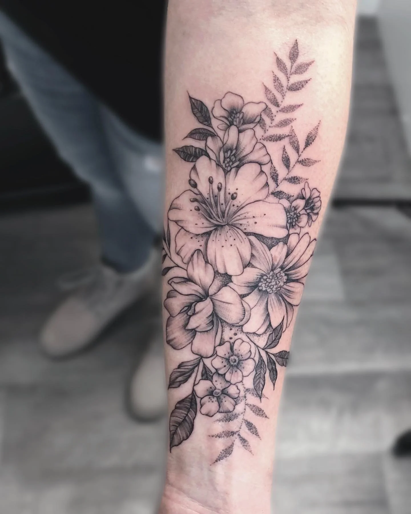 Black and gray floral tattoo featuring various flowers and leaves on a person's forearm.