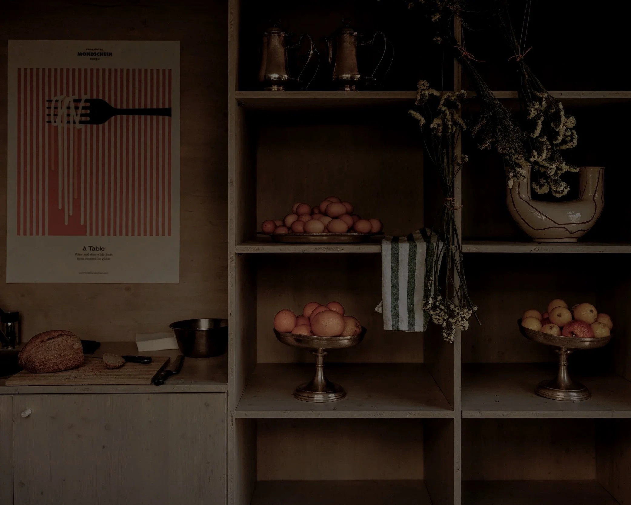 A wooden shelf with flowers and vases, a poster on the wall, and bowls of eggs and apples on the shelves.