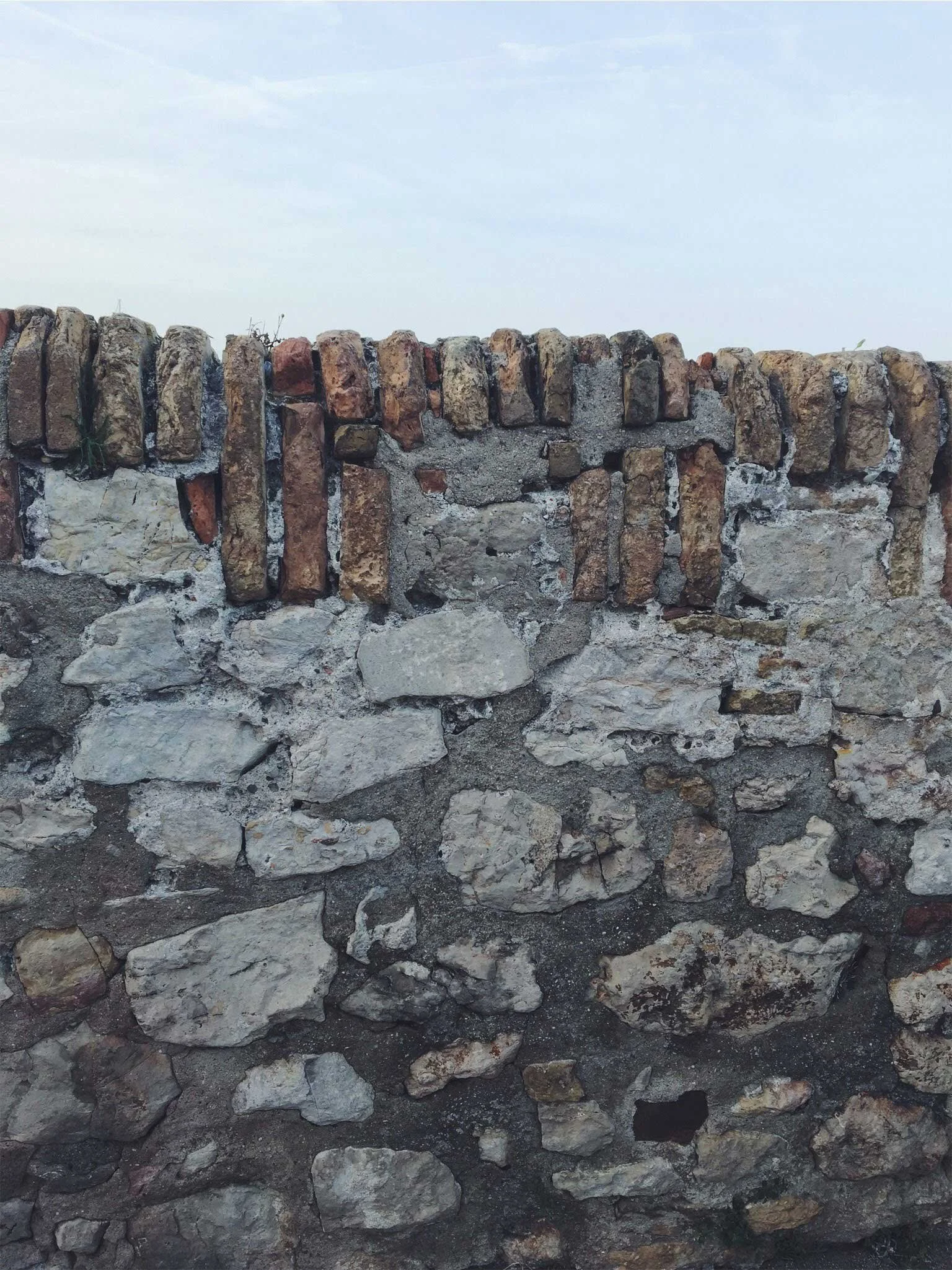 A textured stone wall composed of irregularly shaped stones and bricks against a clear sky backdrop