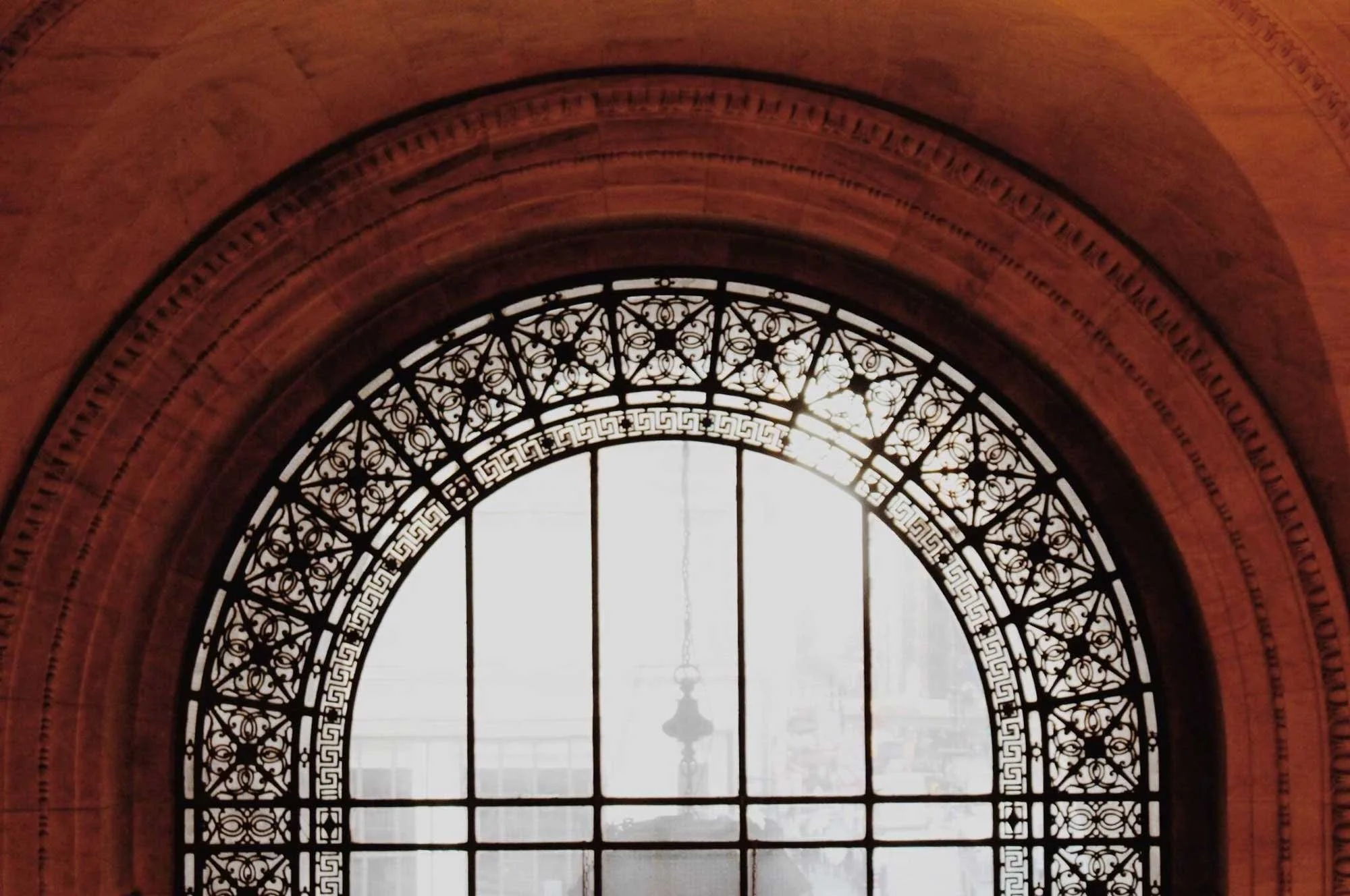 A large, ornate arched window set within a grand stone wall with intricate metalwork design framing the glass 