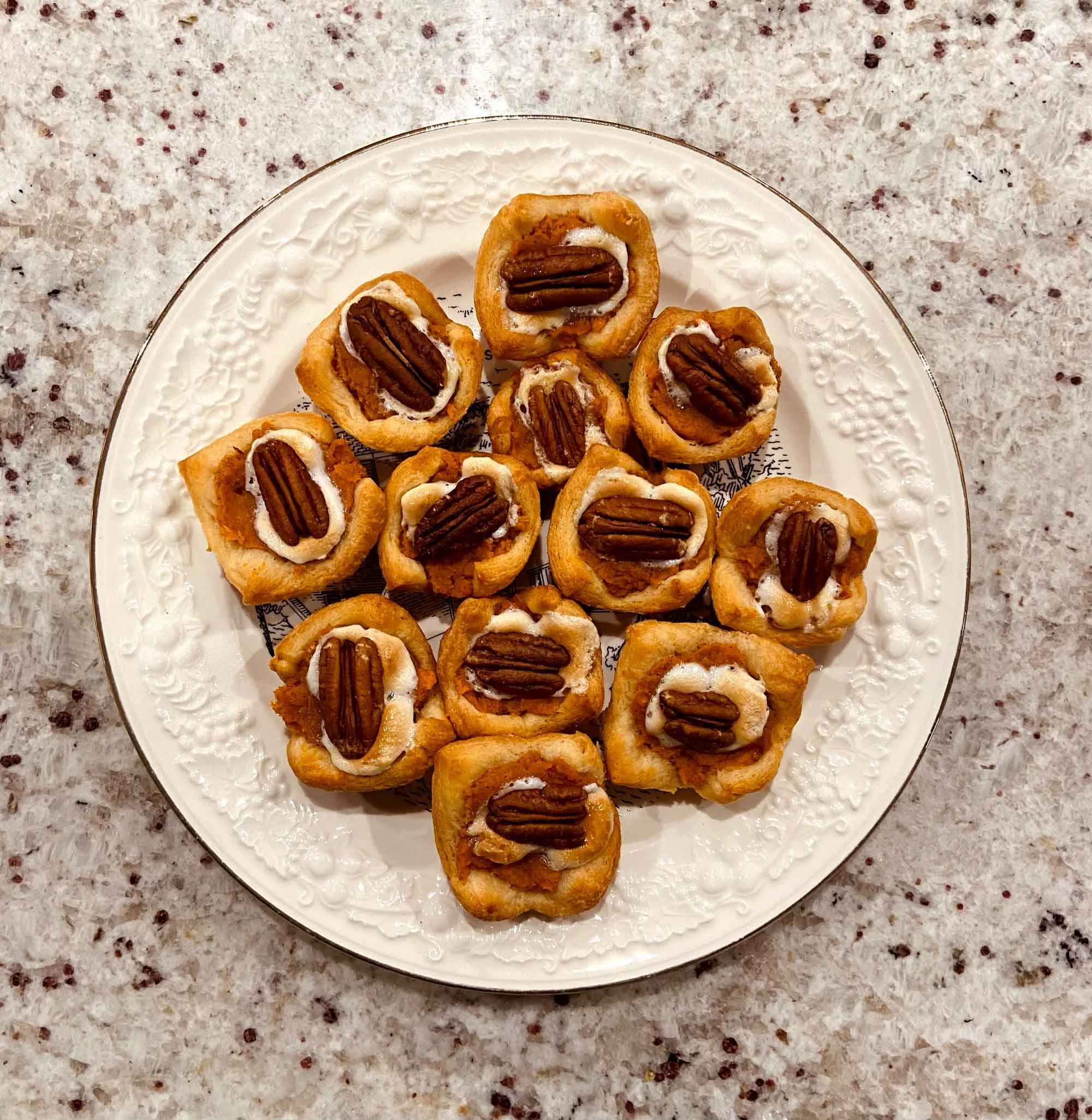 White, decorative plate of bite-sized puff pastry squares, each topped with a toasted pecan and marshmallow