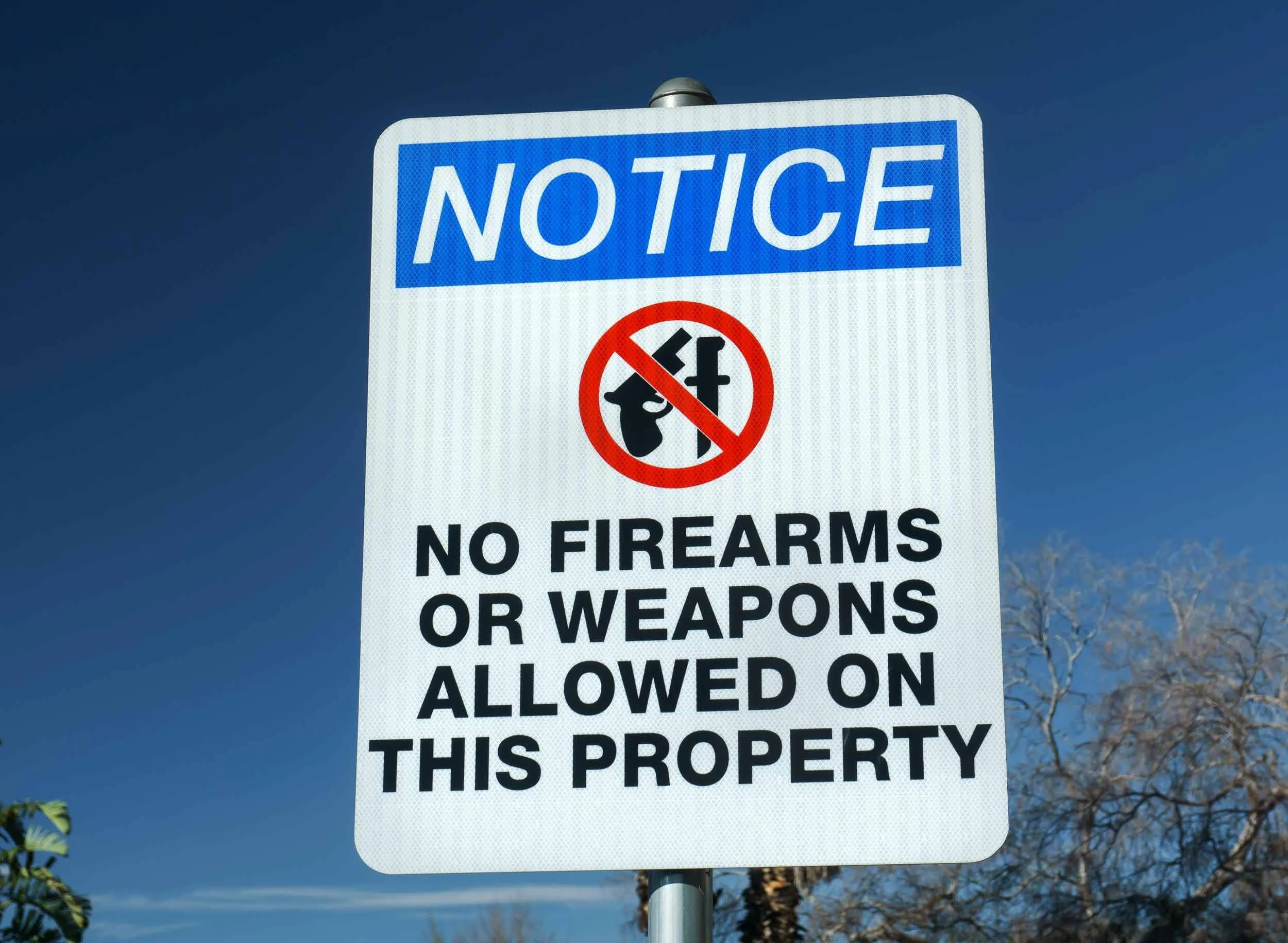 A sign with a red circle with a line through it over a firearm and knife symbol, and text stating "NO FIREARMS OR WEAPONS ALLOWED ON THIS PROPERTY."