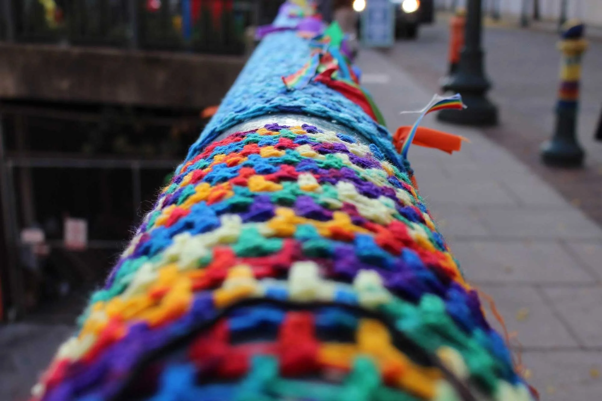 Close-up of a colorful knit cover wrapped around a rail on a sidewalk