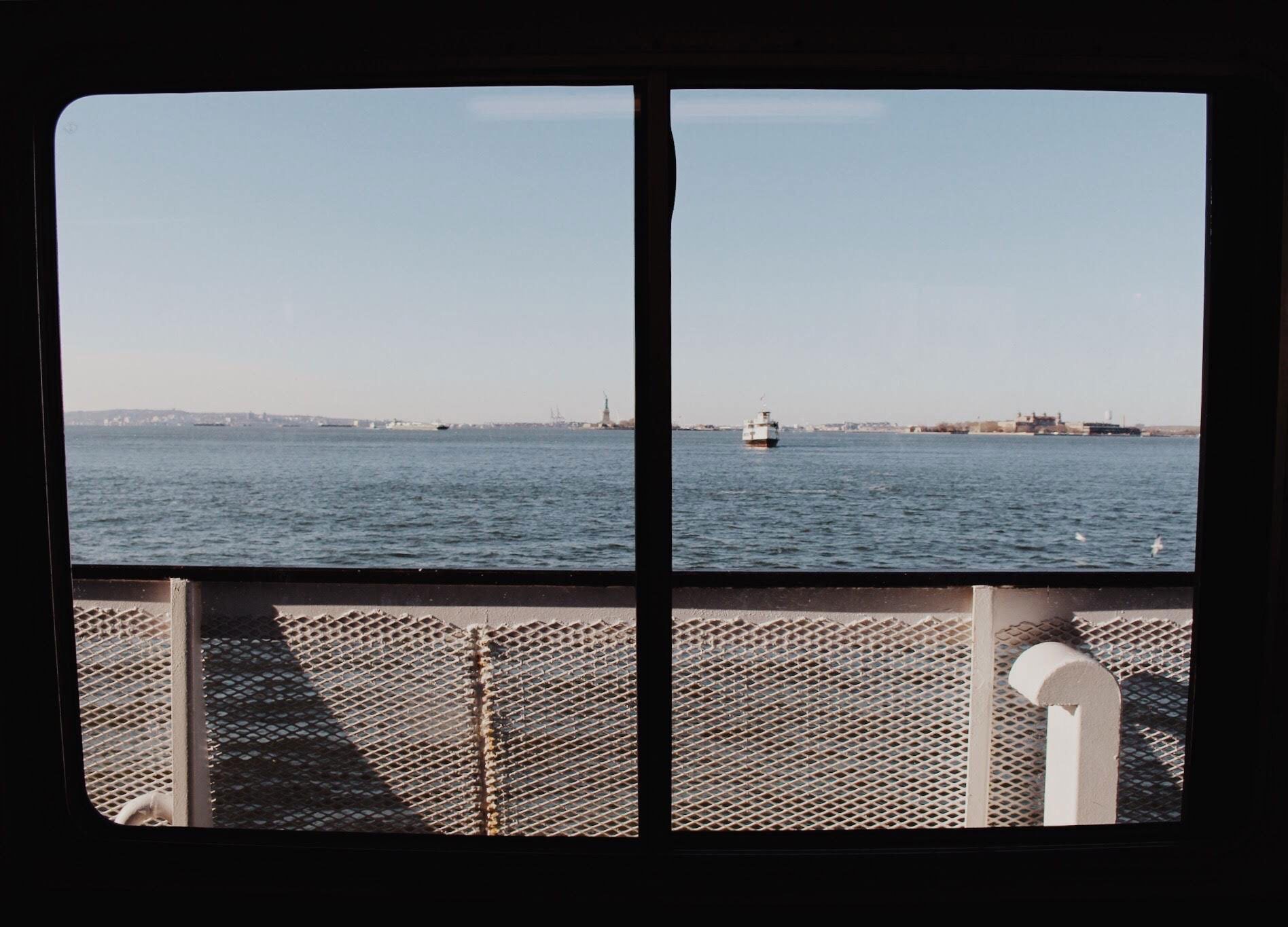 Distant view of the Statue of Liberty and Ellis Island through a ferry window on calm water