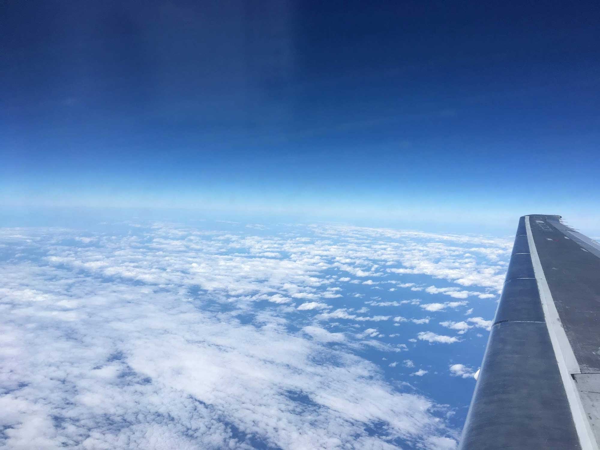 A scenic view from an airplane window showing a vast expanse of white clouds below and a clear blue sky above