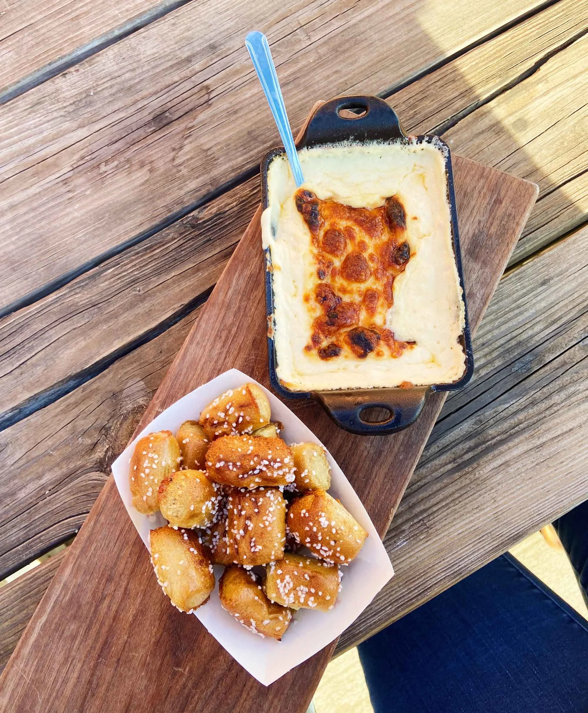 Pretzel bites in white paper container and small cast iron dish of golden-brown baked cheese dip