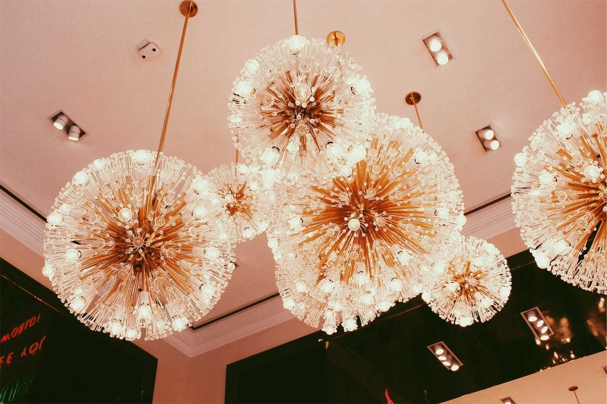 A ceiling adorned with multiple chandeliers composed of golden rods and spherical arrangements of white bulbs, creating a radiant and luxurious atmosphere