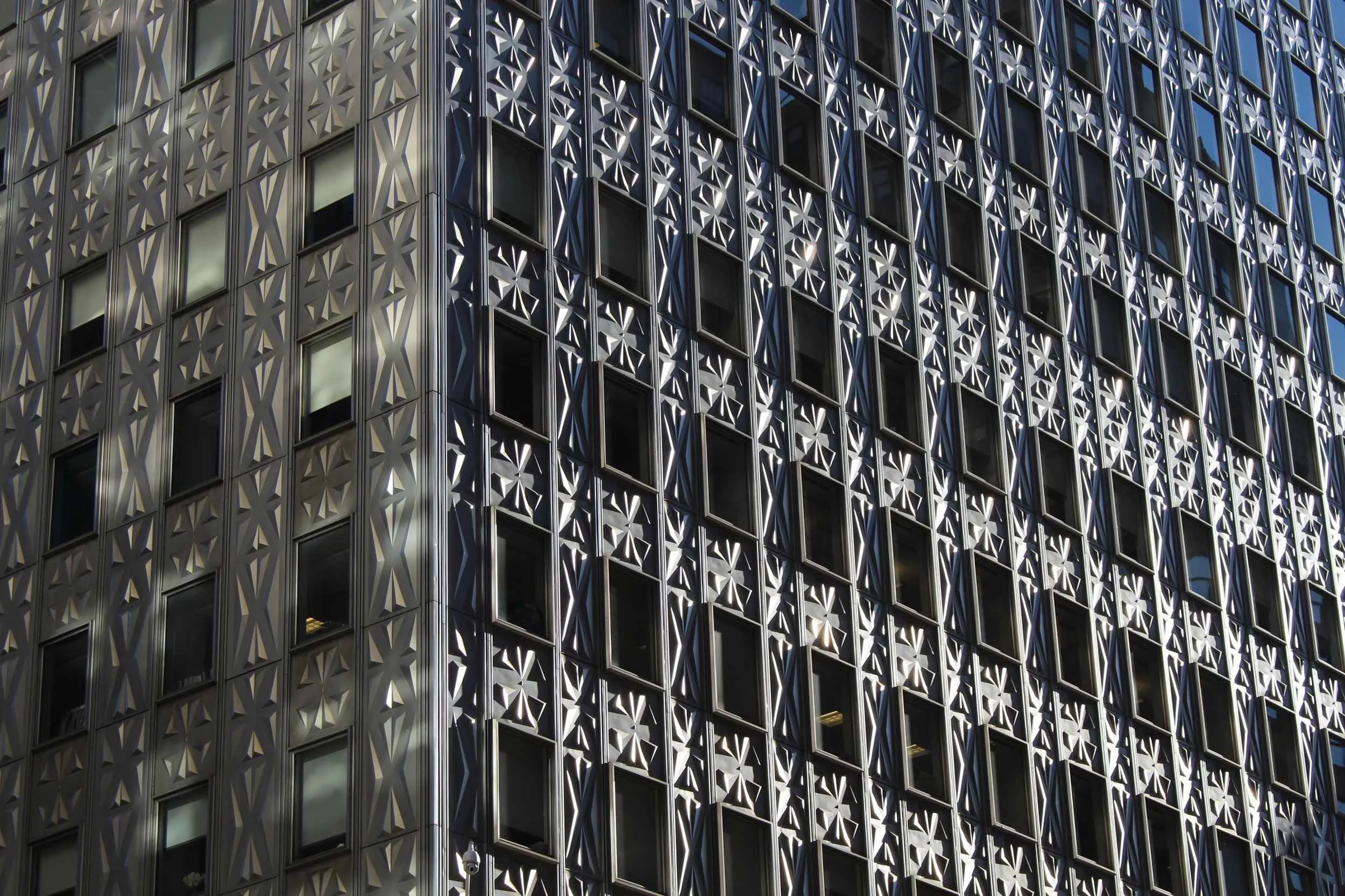 Close-up of the facade of a modern skyscraper, featuring a pattern of rectangular windows set within an intricate, geometric metallic lattice