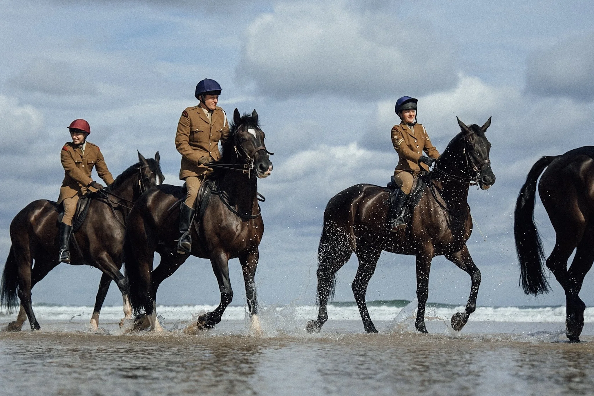 Household cavalry soldiers riding horses through the surf on northumberland beach