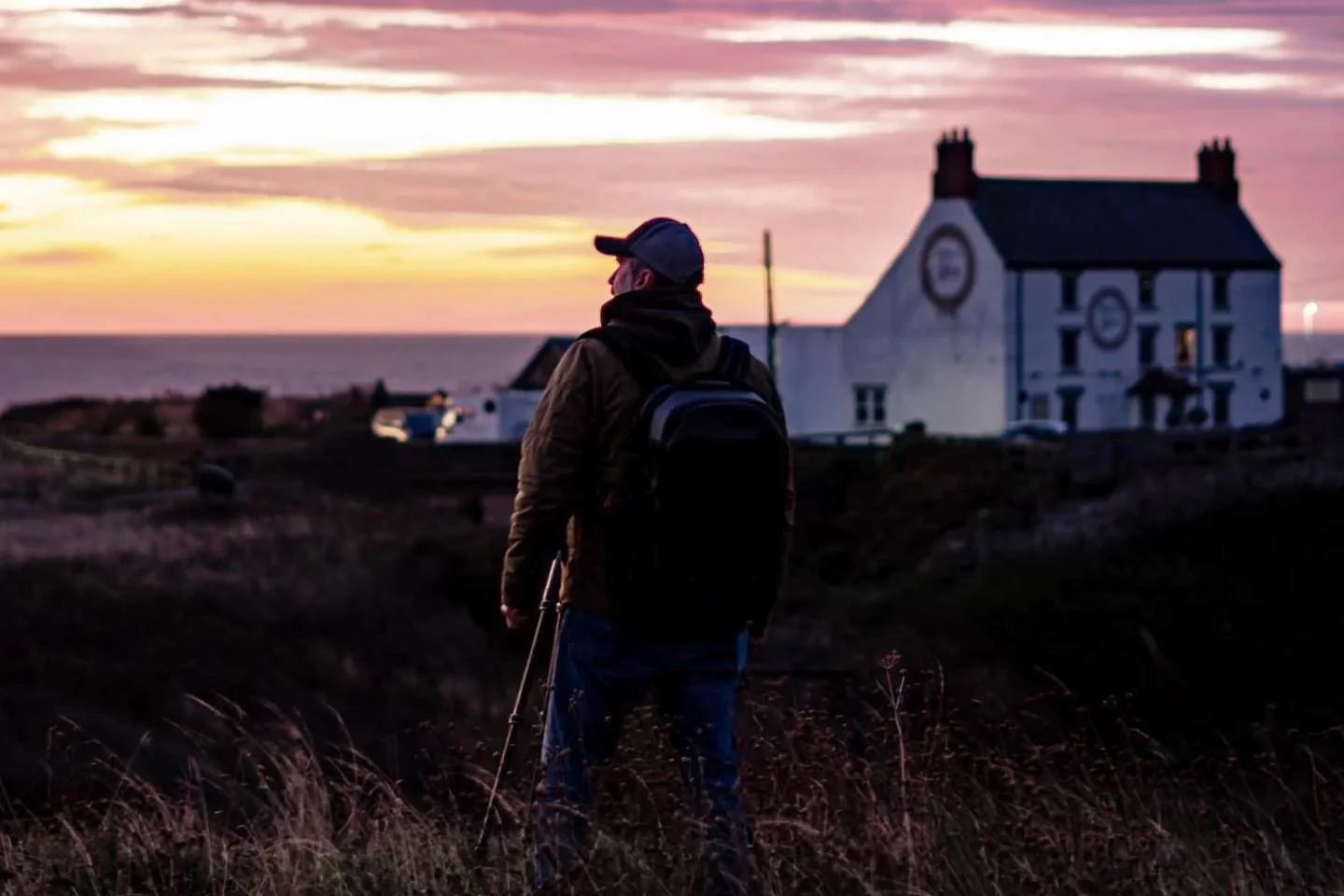 Man standing in field looking out at sunrise with white building in the background