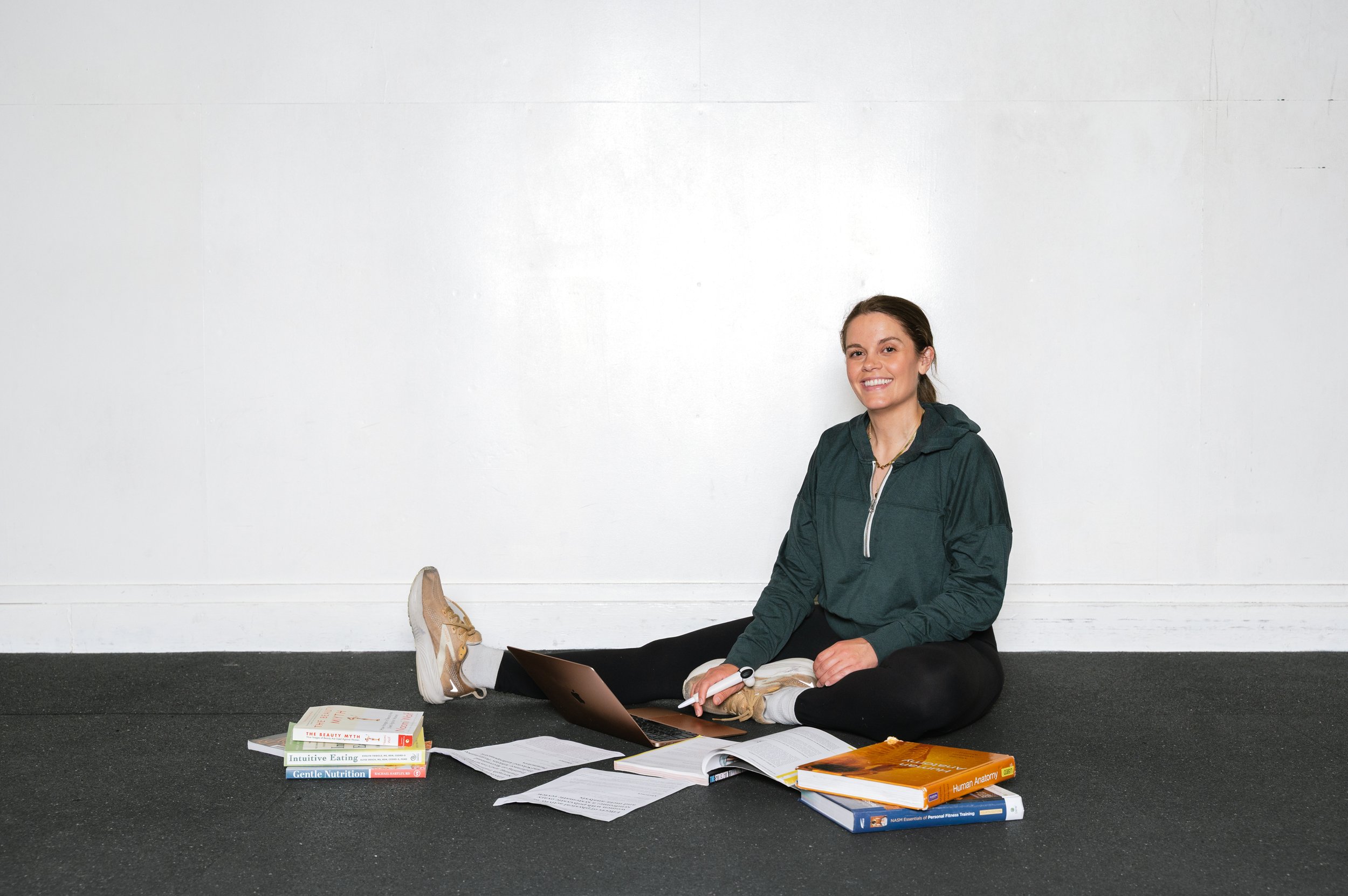 Allison Mosso sitting down looking at the camera, she's surrounded by books on nutrition, intuitive eating, anatomy, and her laptop.