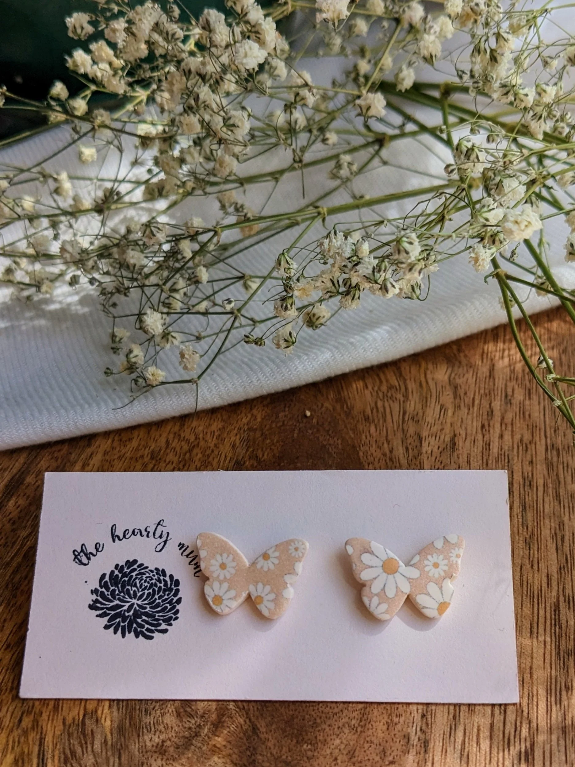 Handcrafted polymer clay earrings. Tan butterfly with white and yellow flower print. All components are gold plated, silver plated, or stainless steel with sensitive ears in mind.