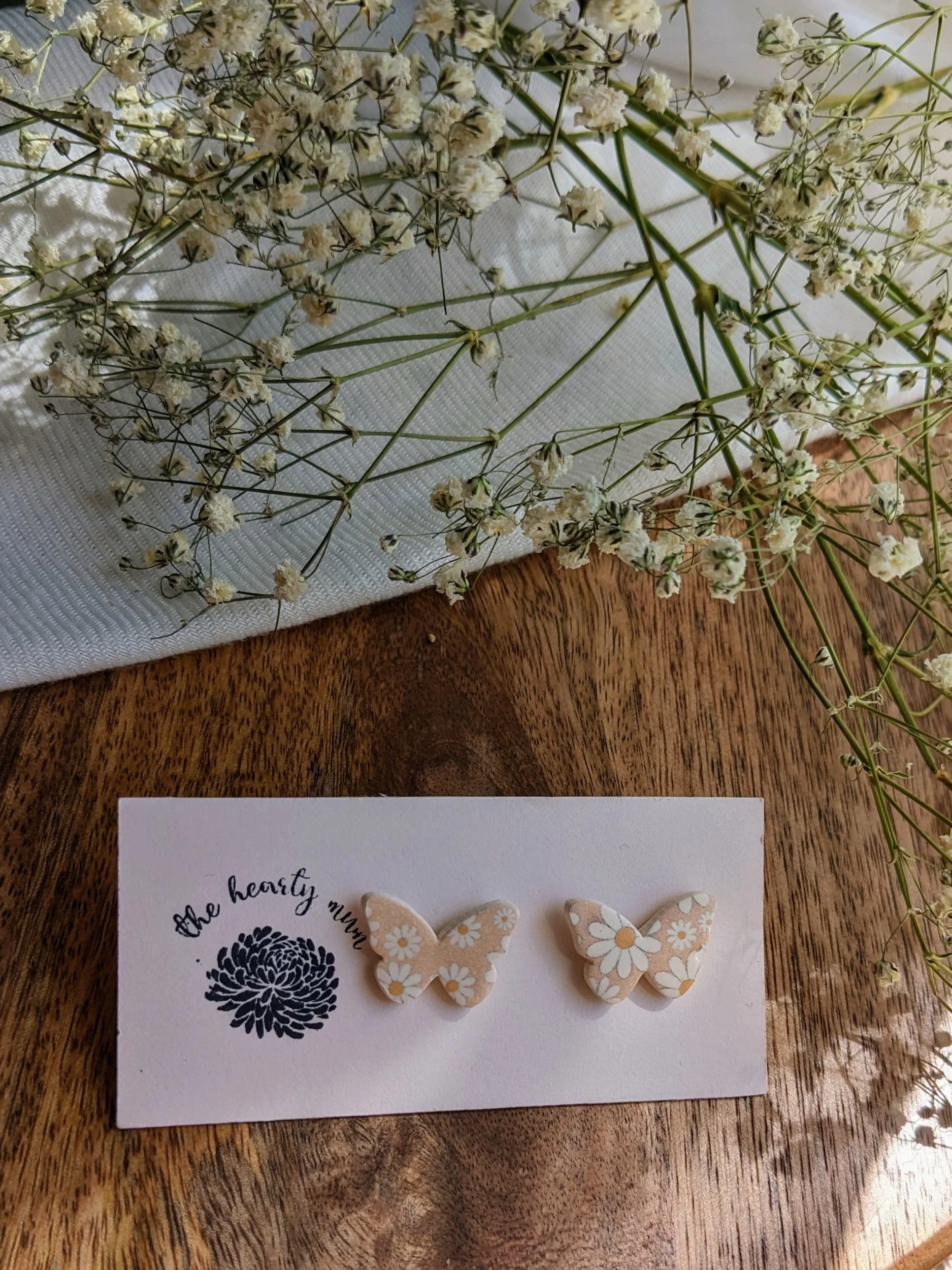 Handcrafted polymer clay earrings. Tan butterfly with white and yellow flower print. All components are gold plated, silver plated, or stainless steel with sensitive ears in mind.