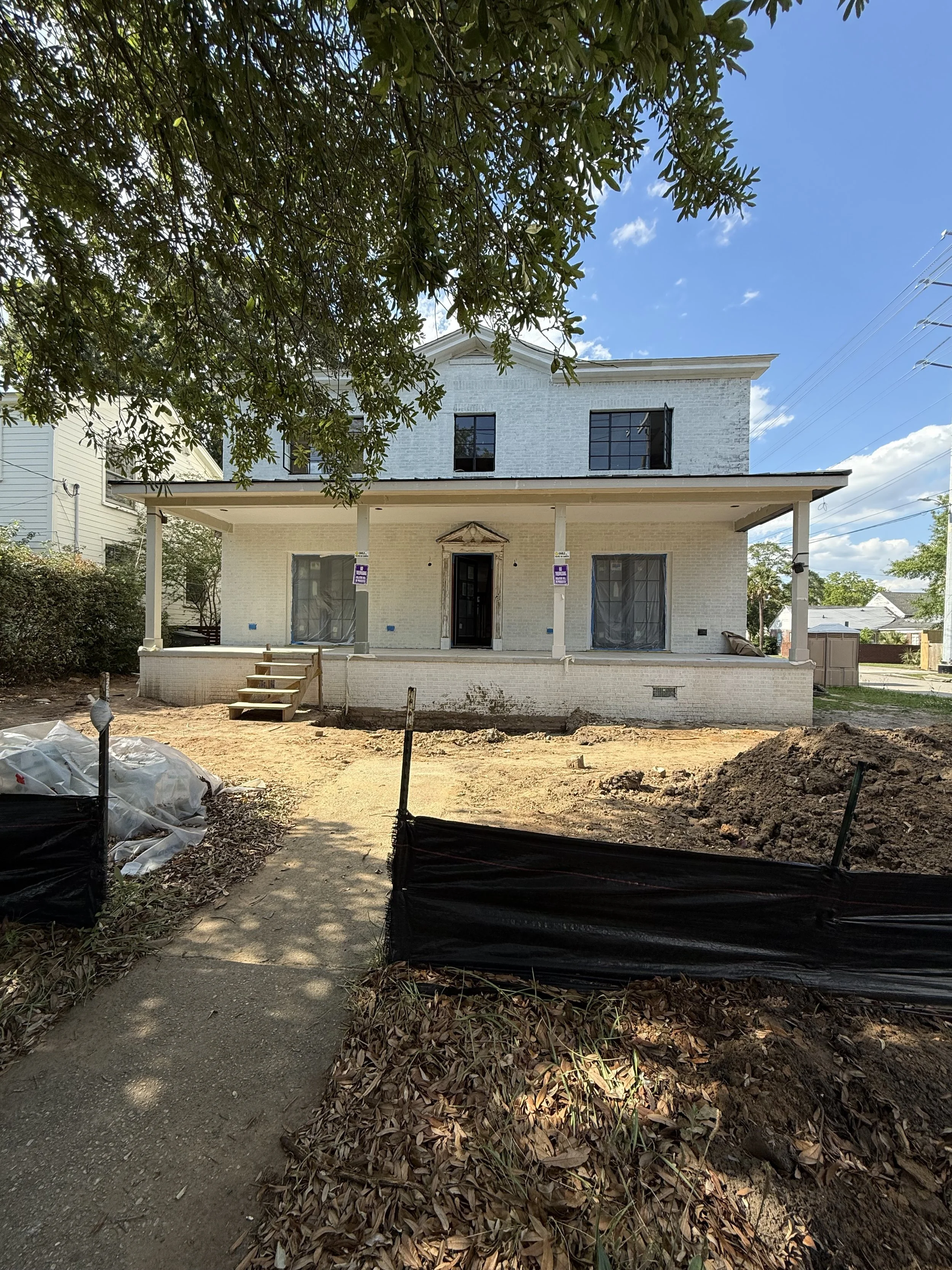 Under construction white two-story house with a front porch, stairs, and plastic-covered windows, surrounded by dirt and leaves on a sunny day.