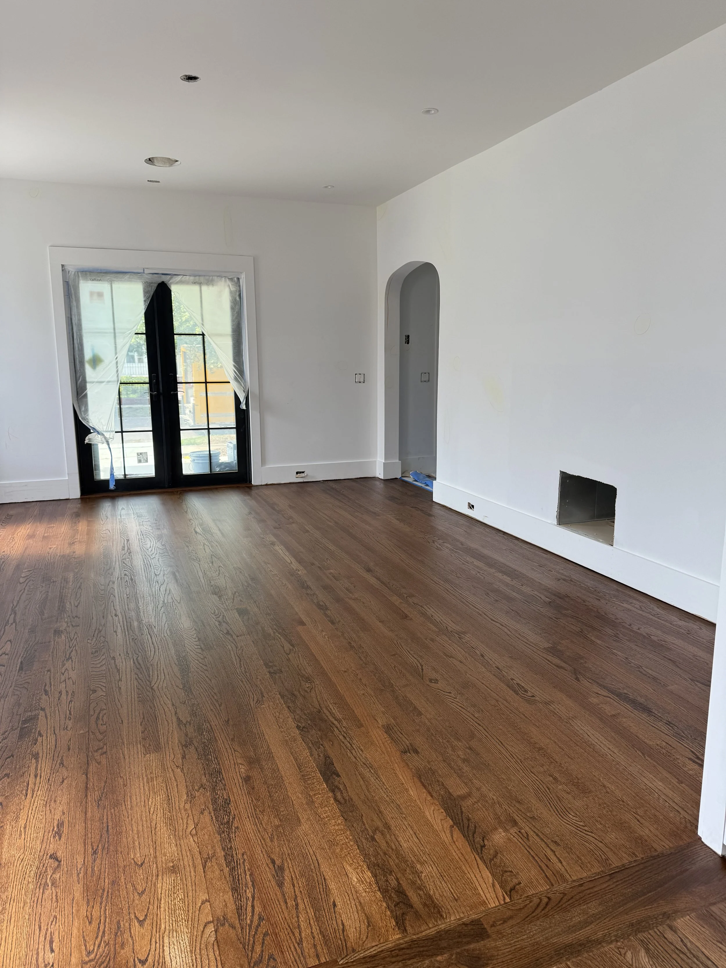 Empty living room with hardwood floors, white walls, and a sliding glass door covered with curtains.