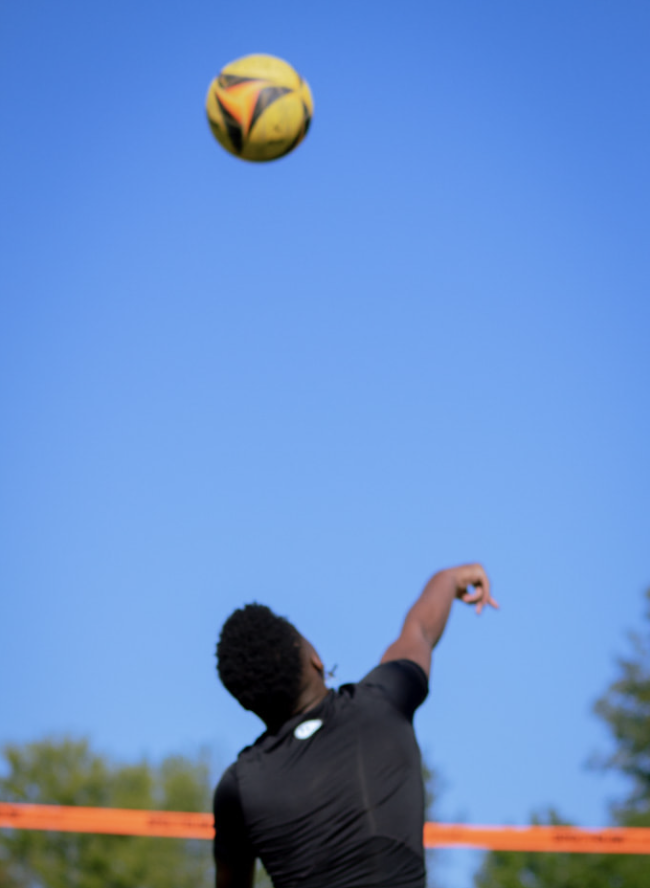 Man serving a volleyball with a blue sky