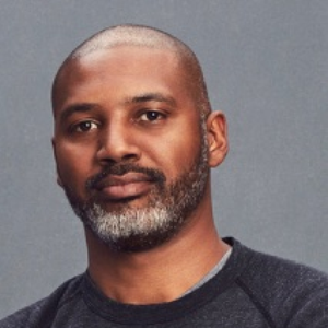 A headshot of a Black man with a beard, wearing a black heathered sweatshirt