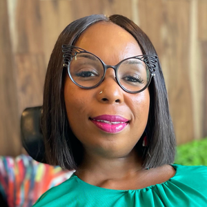 A headshot of a smiling Black woman with her hair in a bob, wearing cat eye glasses and a green silky top