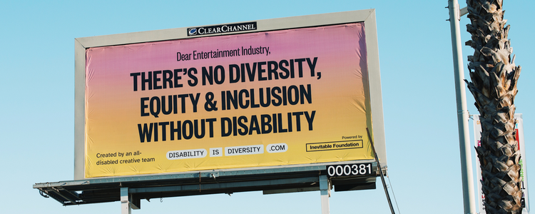 A photograph of a billboard against a blue sky and next to the trunk of a palm tree. The poster is a pink and yellow gradient with bold text that reads: “Dear Entertainment Industry, There’s no diversity, equity & inclusion without disability.”