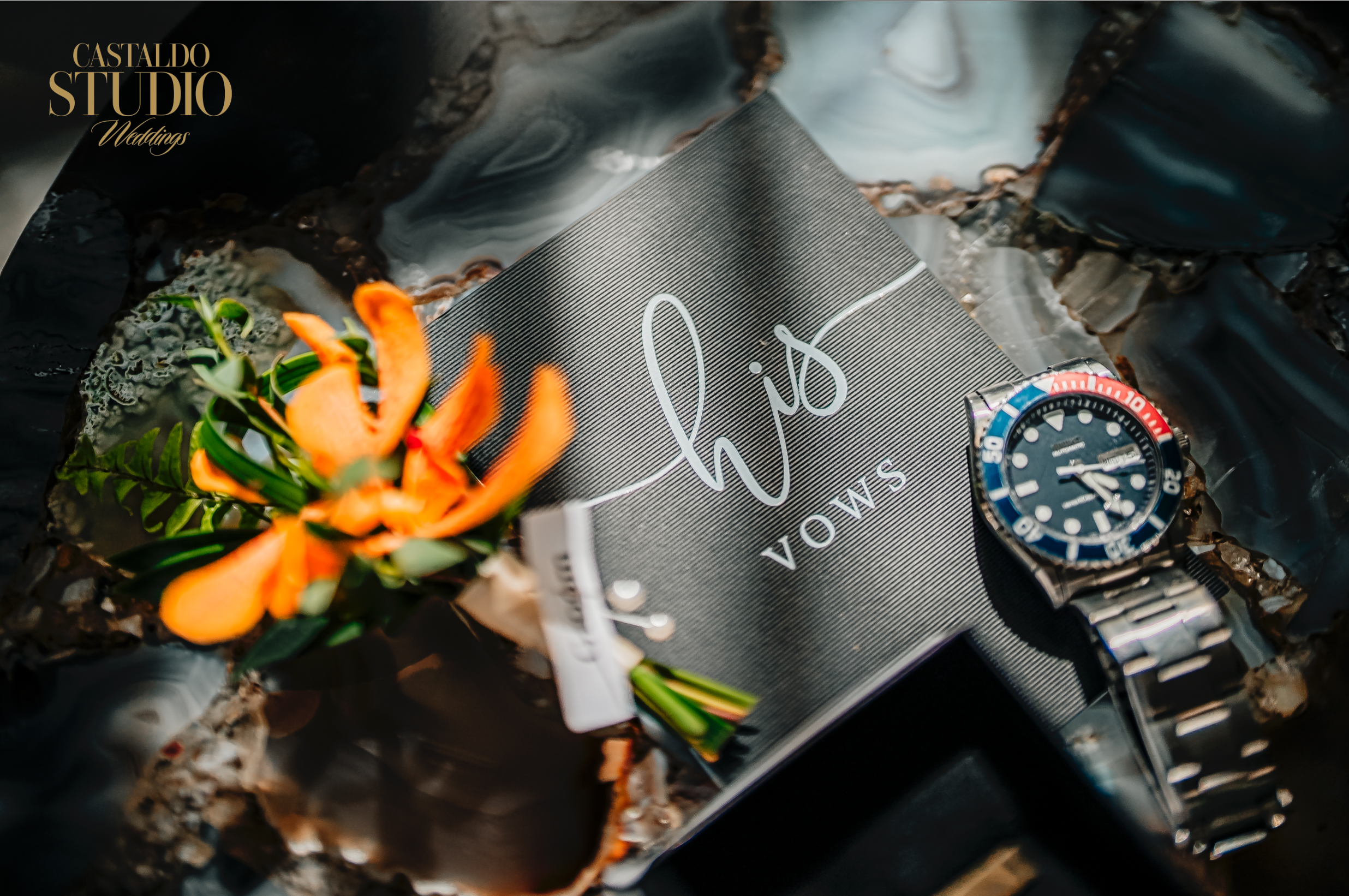 Wedding detail flat lay of groom's "His Vows" book, orange orchid boutonniere, and watch at a destination wedding at Paradise Cove Orlando, photographed by Castaldo Studio Weddings.