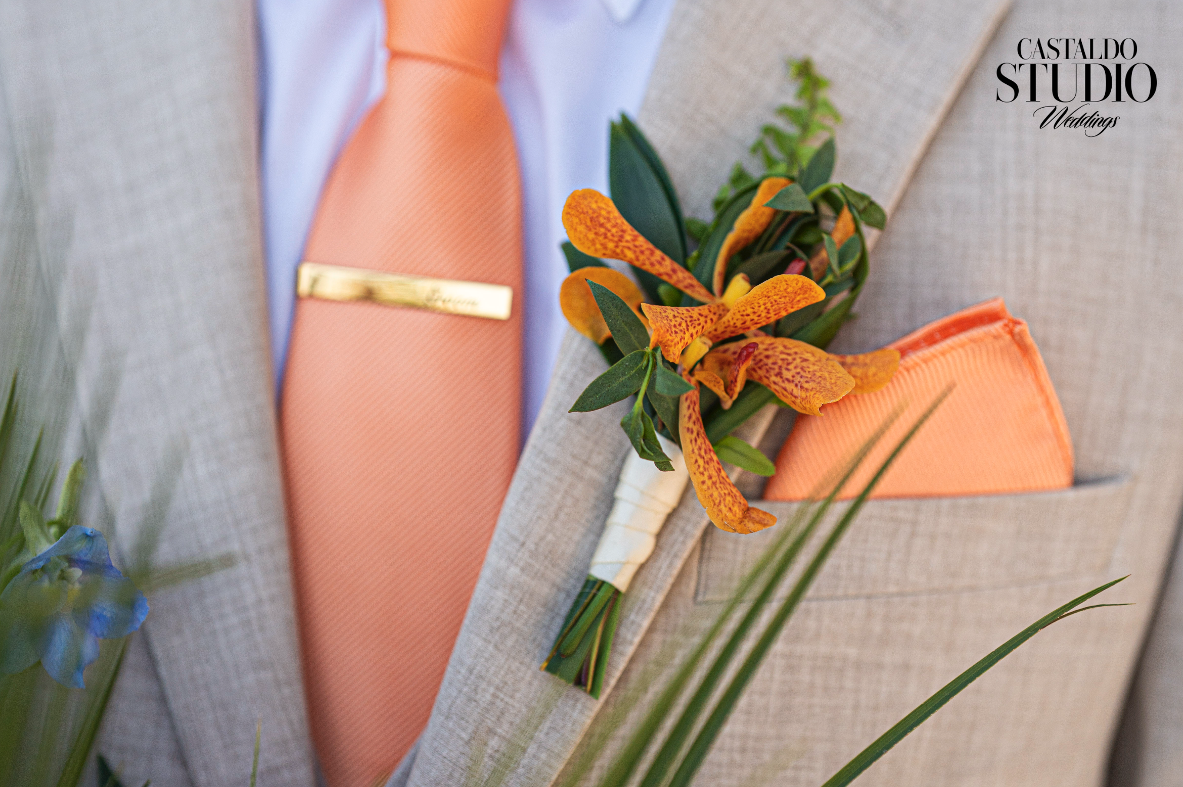 Close-up of groom's orange orchid boutonniere and peach tie with gold tie clip at Paradise Cove Orlando destination wedding, photographed by Castaldo Studio Weddings.