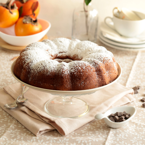 Persimmon Pudding Cake dusted with powdered sugar rested on a pedestal dessert plate.
