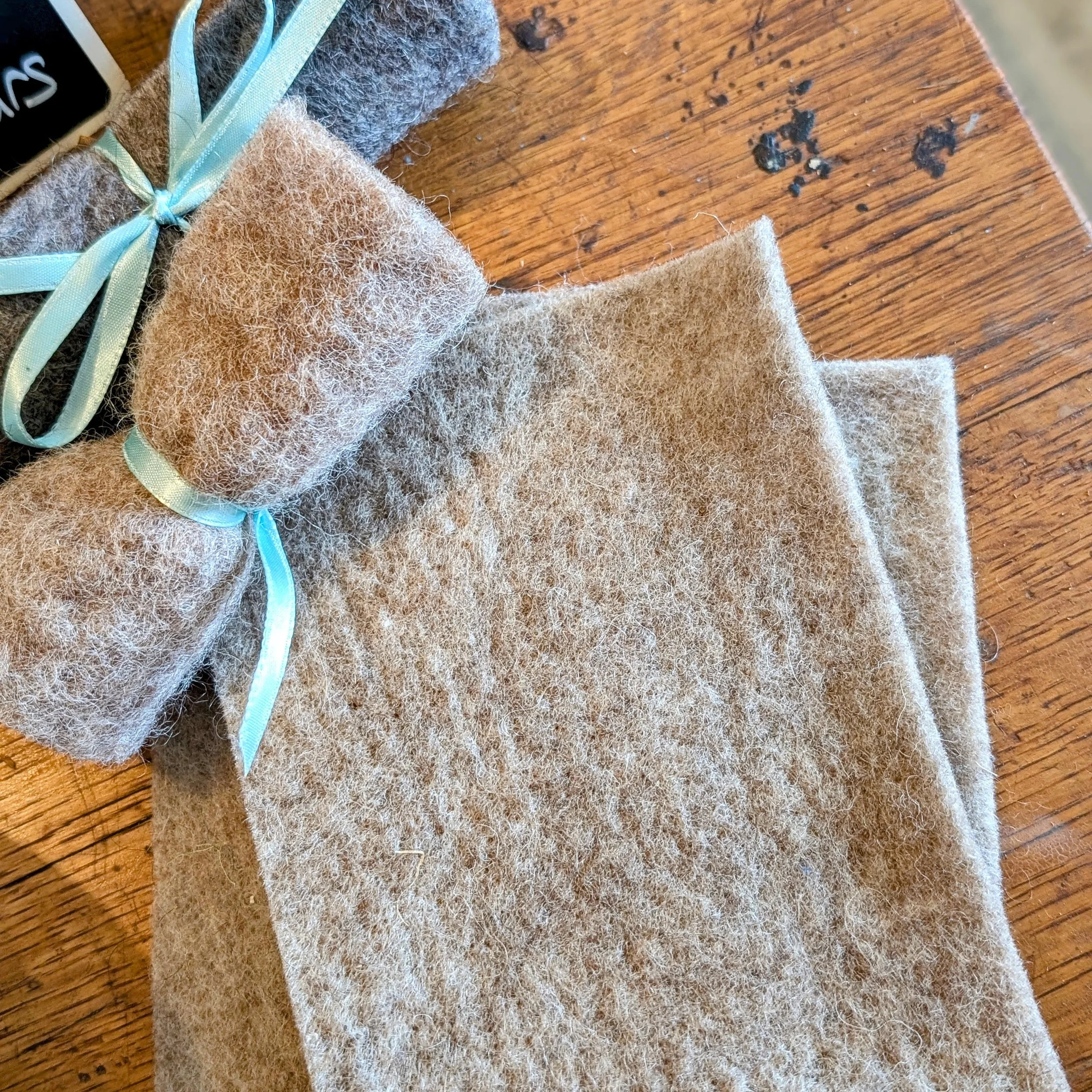 Close-up of fuzzy beige fabric swatches with light blue ribbons on a wooden surface.