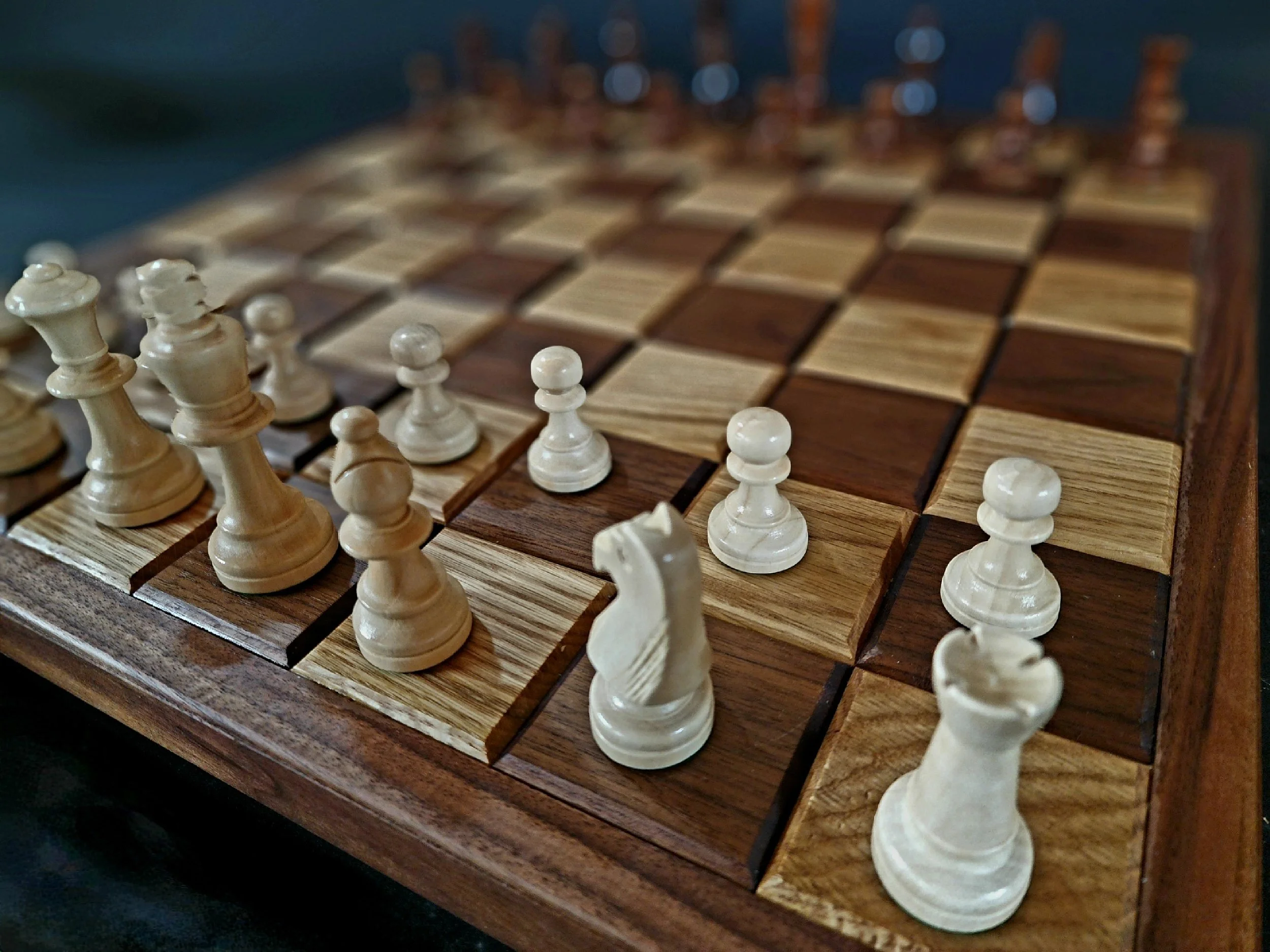 A close-up view of a wooden chessboard with white chess pieces set up for a game.