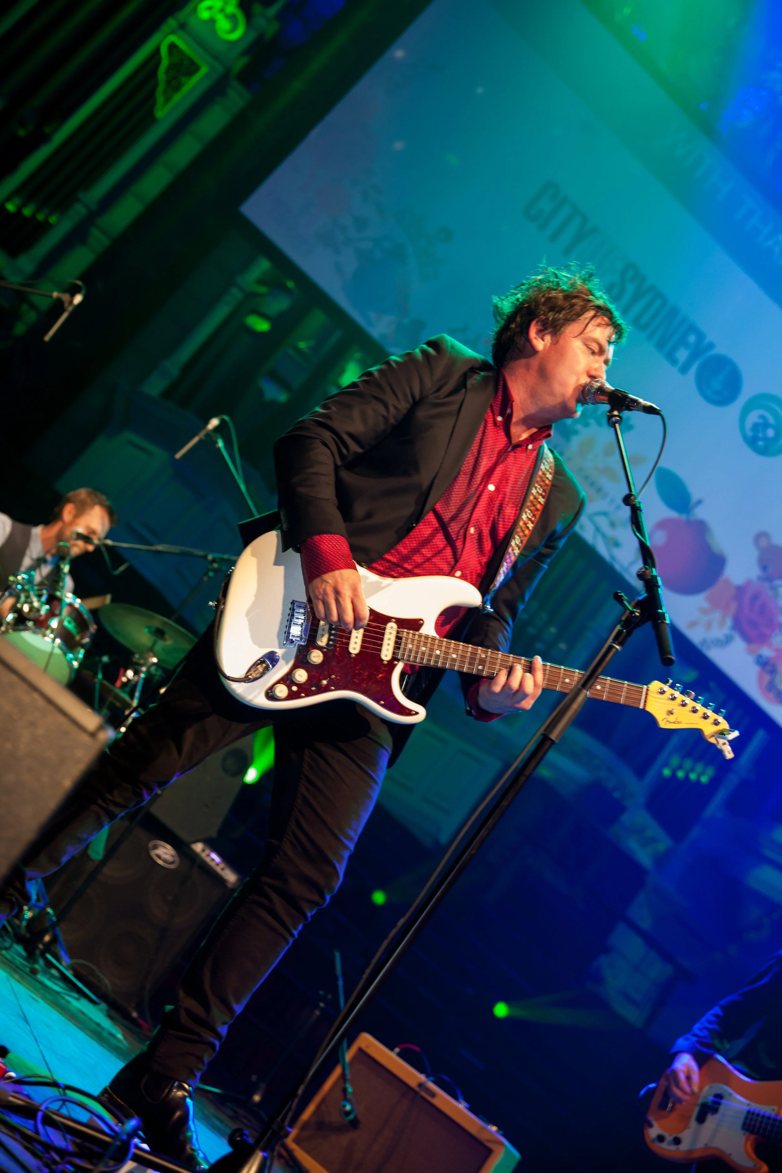 Musician playing electric guitar and singing into microphone on stage at a concert.