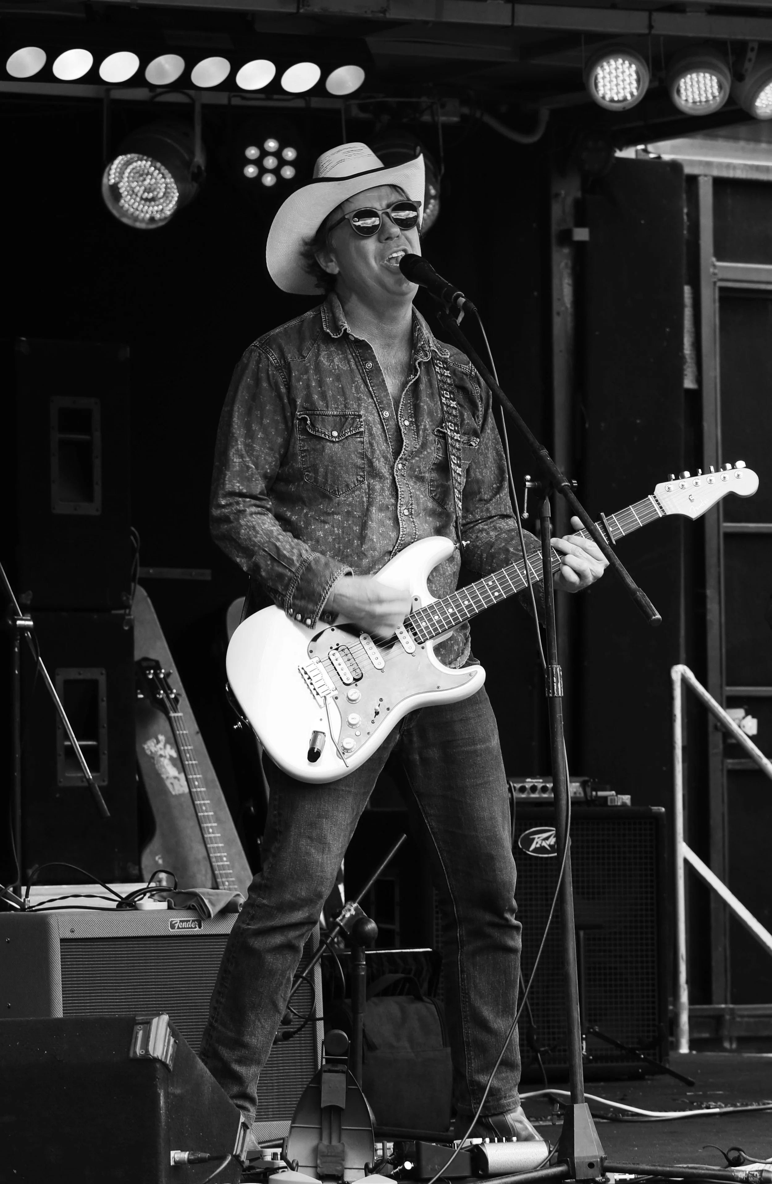 A musician singing into a microphone and playing an electric guitar on a stage.