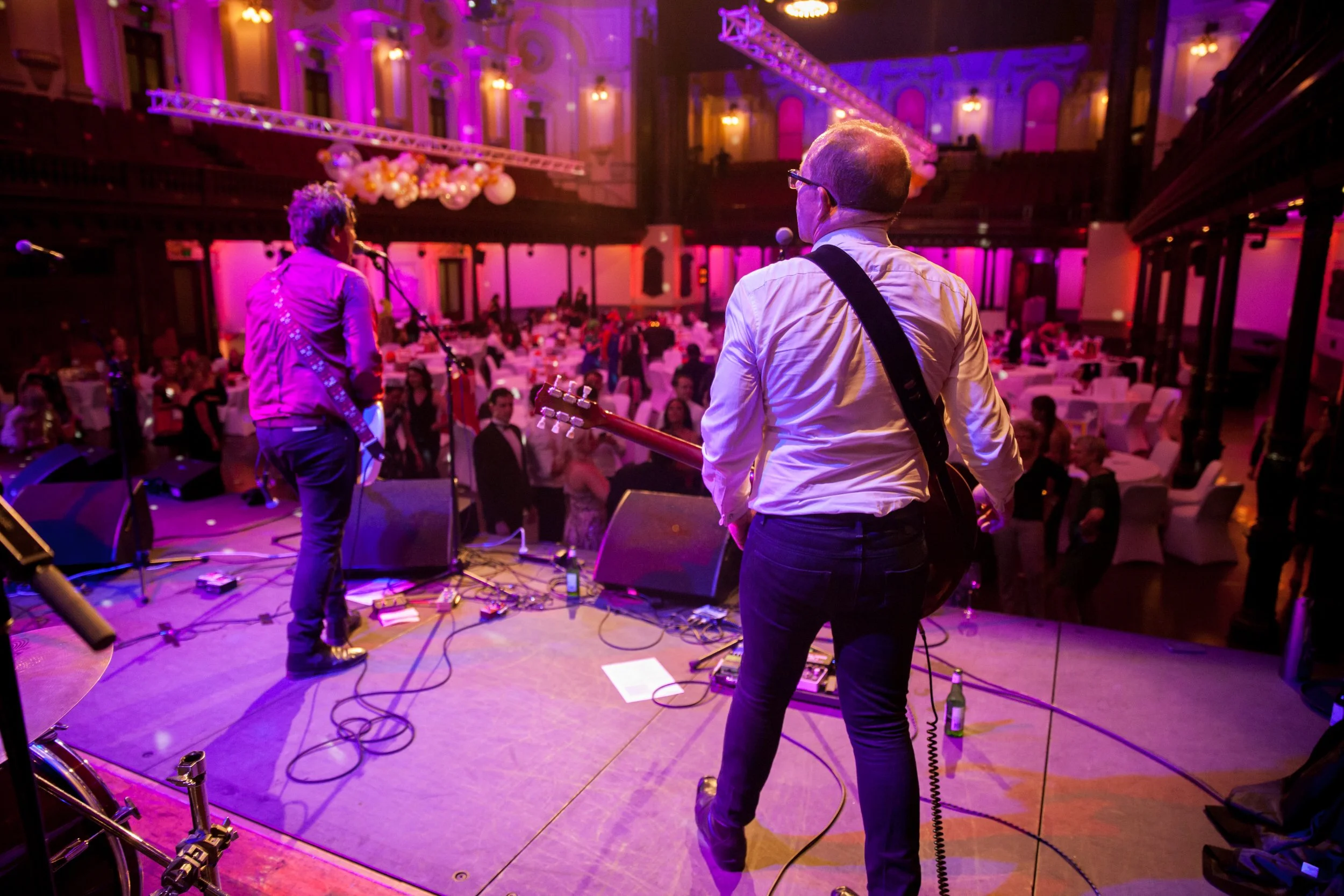 Musicians performing on stage at a large, elegant event hall with purple lighting, surrounded by tables with seated guests.