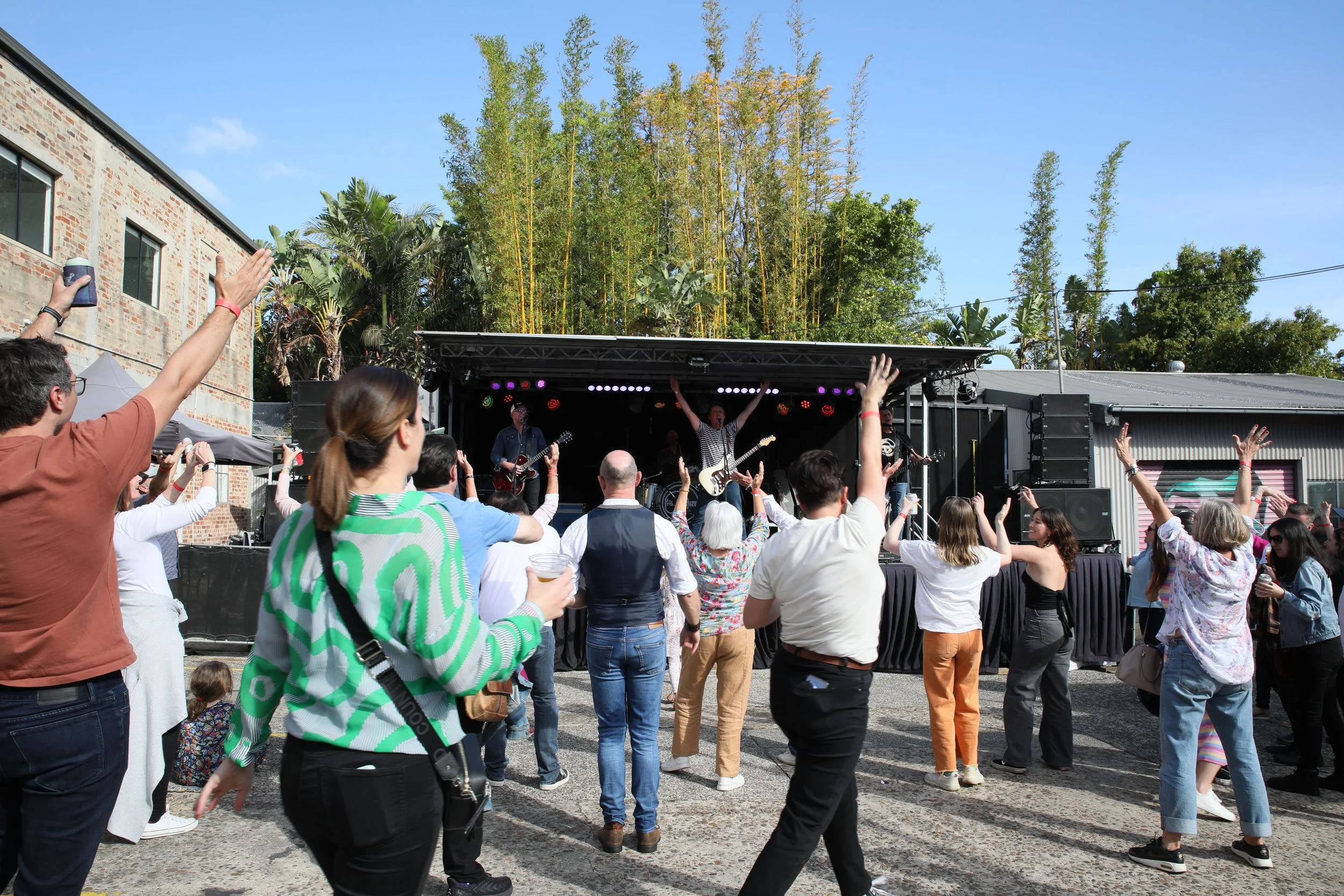 People dancing and enjoying live music on an outdoor stage during the day.