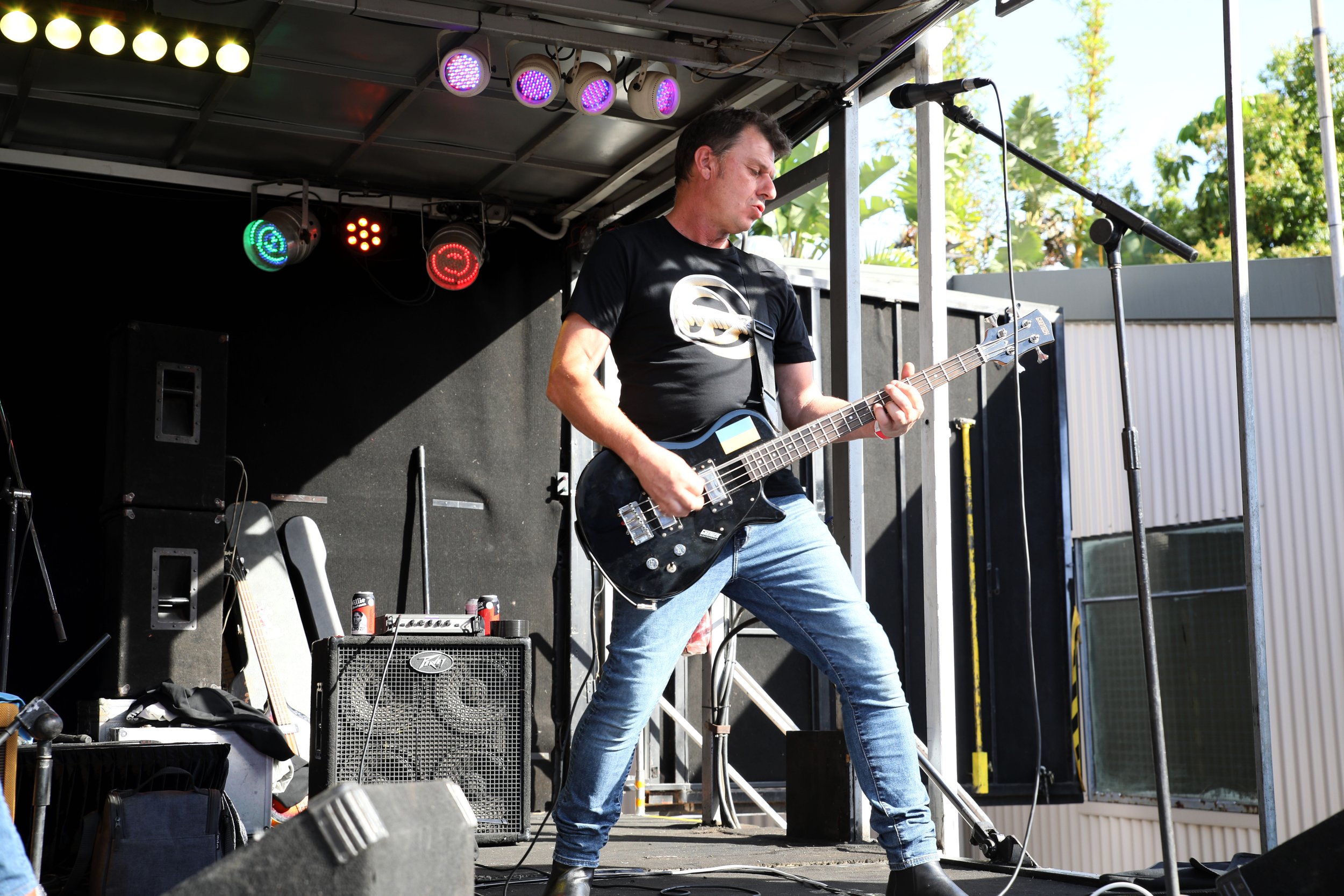 Man playing an electric guitar on stage during an outdoor concert.