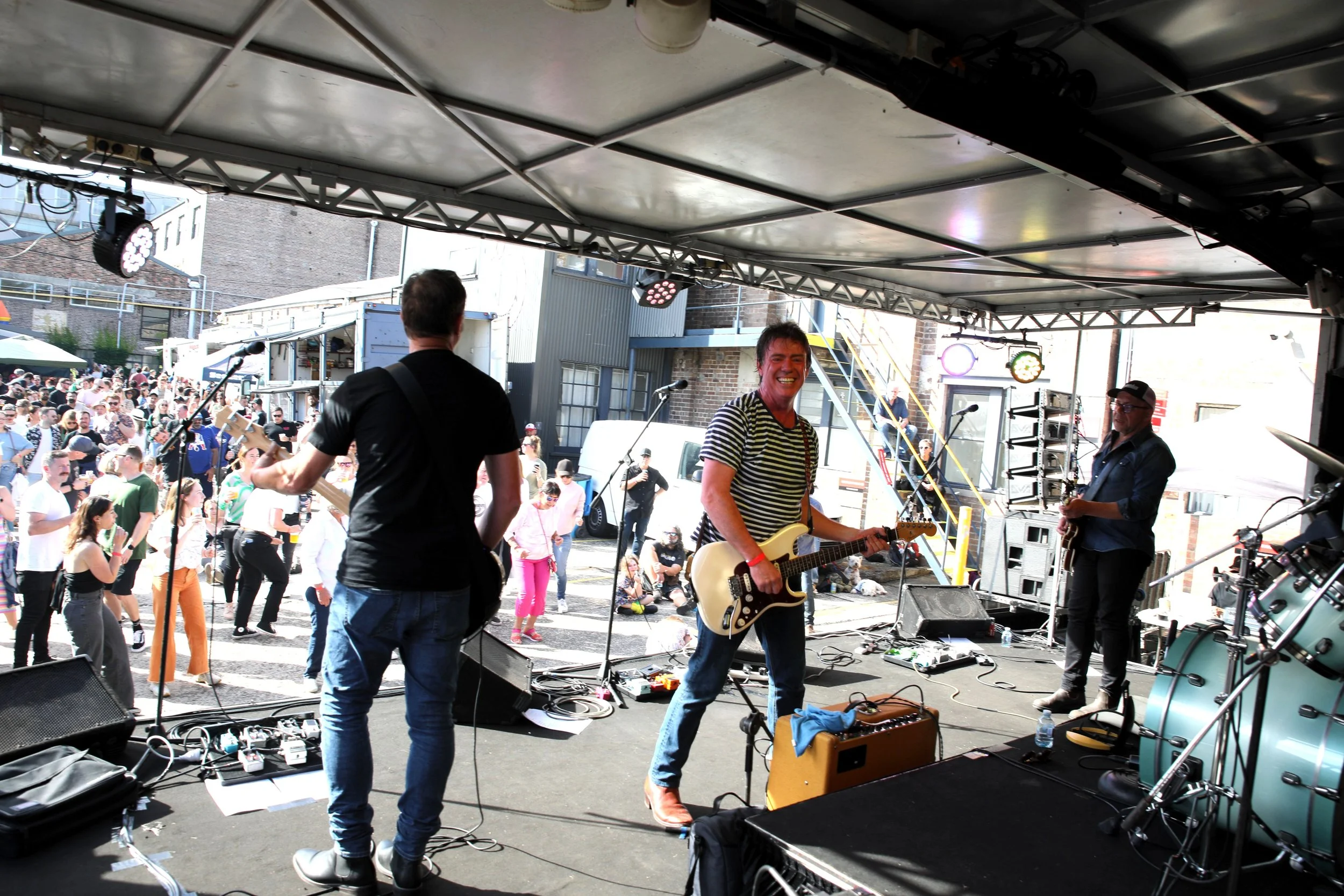 Band performing on stage with an audience in an outdoor setting.