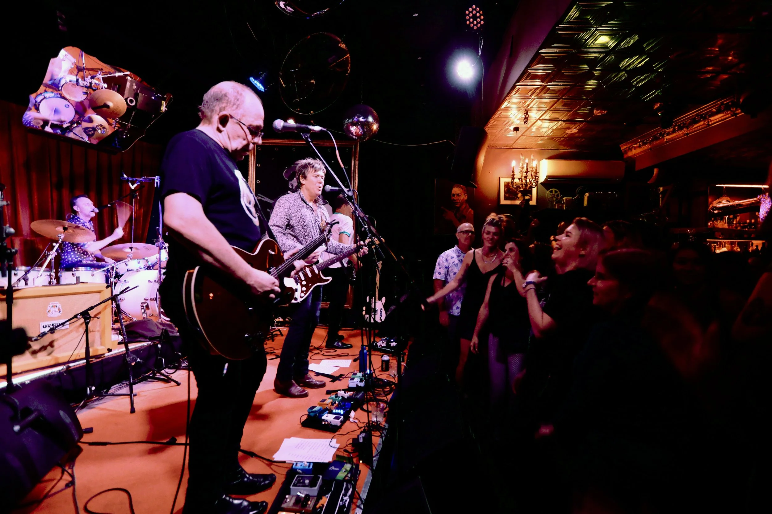 A band performing live on stage at a nightclub, with audience members watching and enjoying the show.