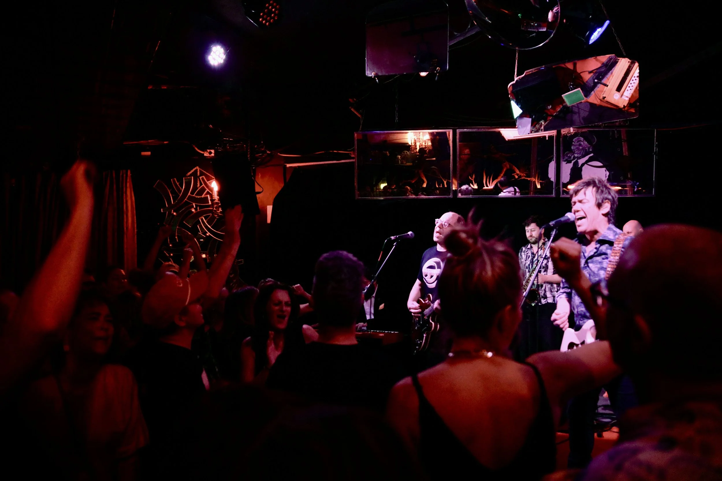 A live music performance at a nightclub with a band on stage, audience dancing and enjoying the show, dim lighting, and colorful stage lights.