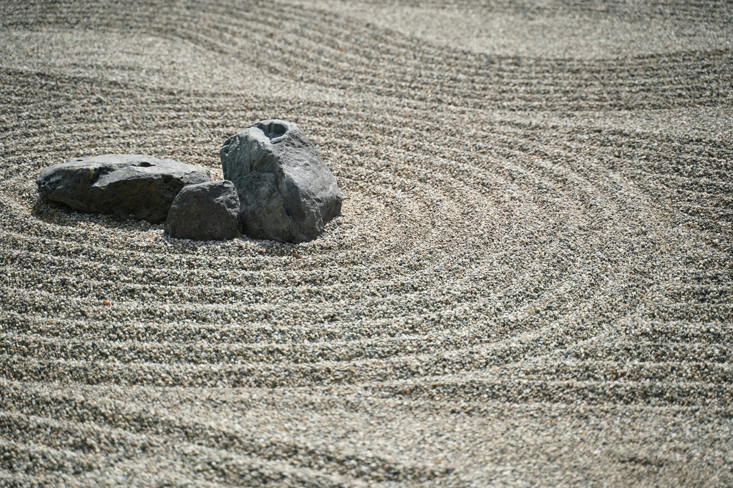 A zen garden with sand raked in circular patterns around three small stones.