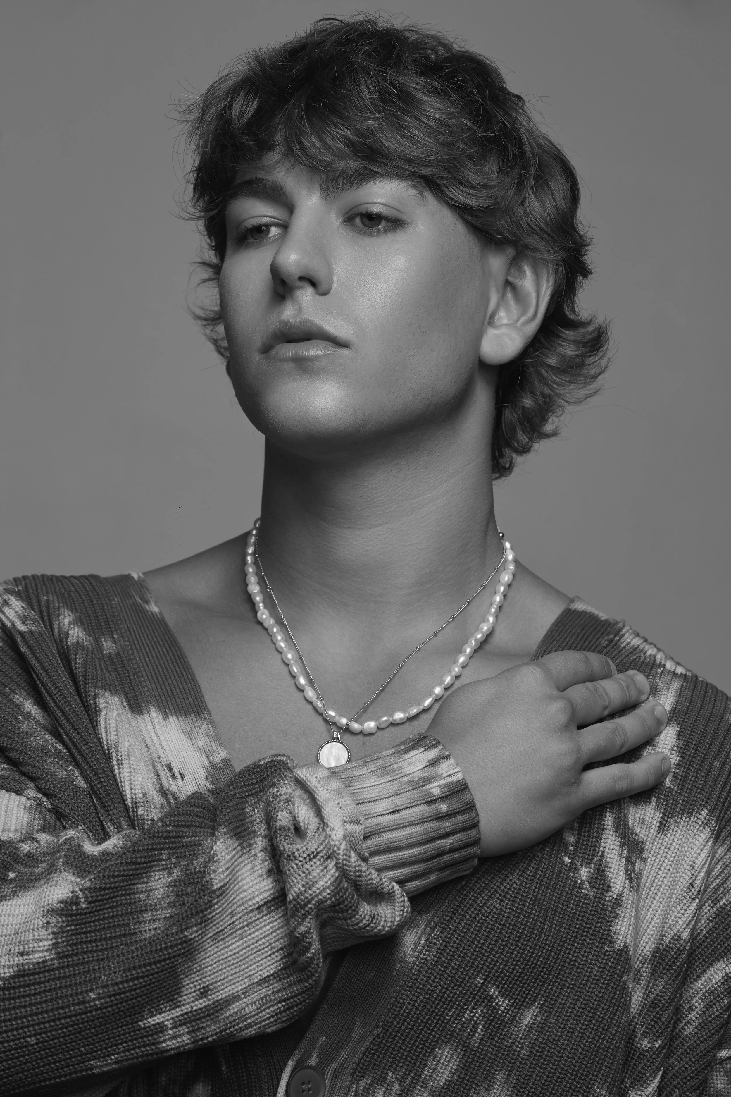 A black and white portrait of a woman with short wavy hair, wearing layered necklaces and a patterned sweater, looking slightly to the side with a calm expression.