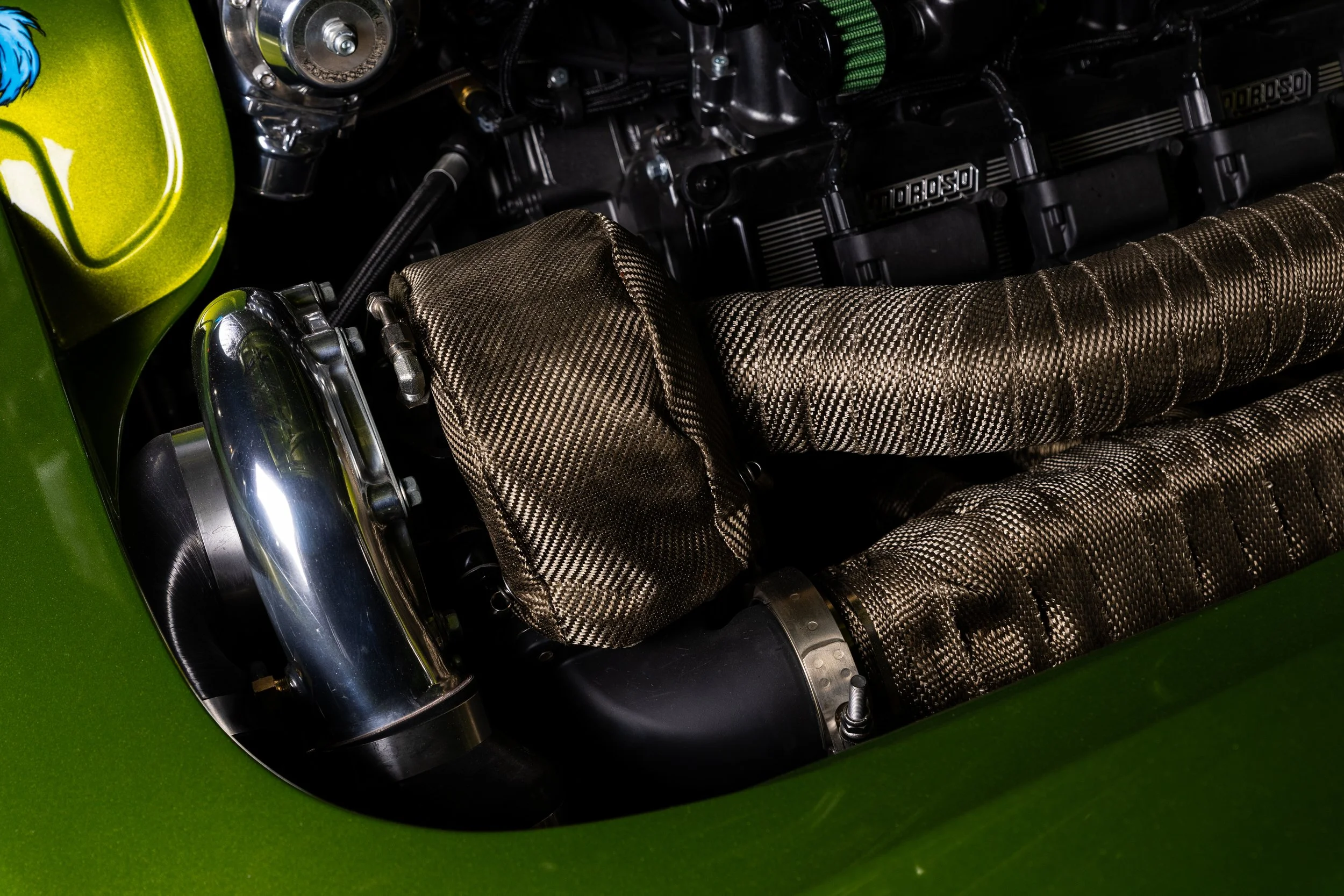 Close-up of a car engine with carbon fiber components and a green exterior.