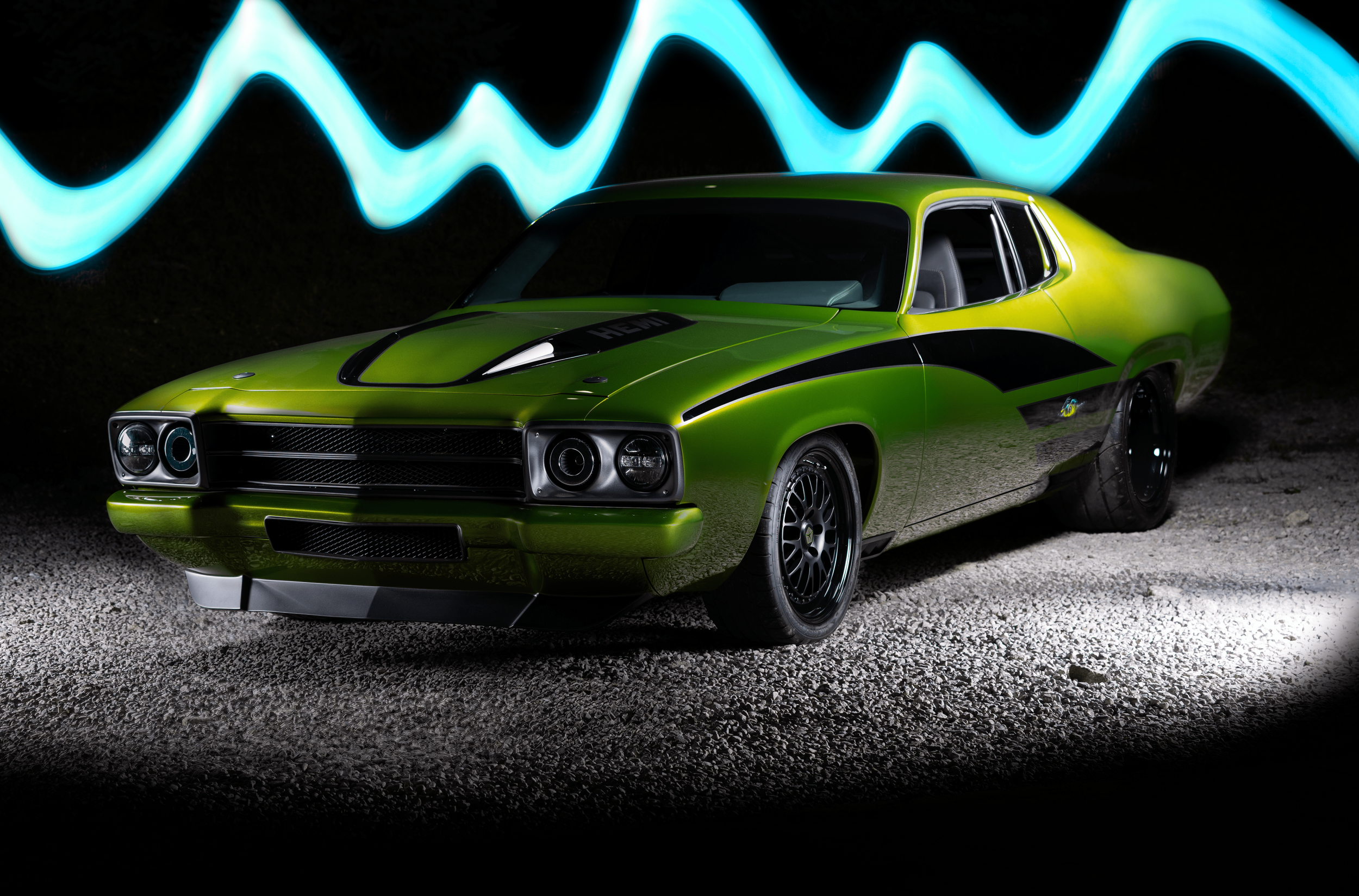 Green vintage muscle car with black racing stripes and modern wheels parked on gravel surface at night with neon light streaks in the background.