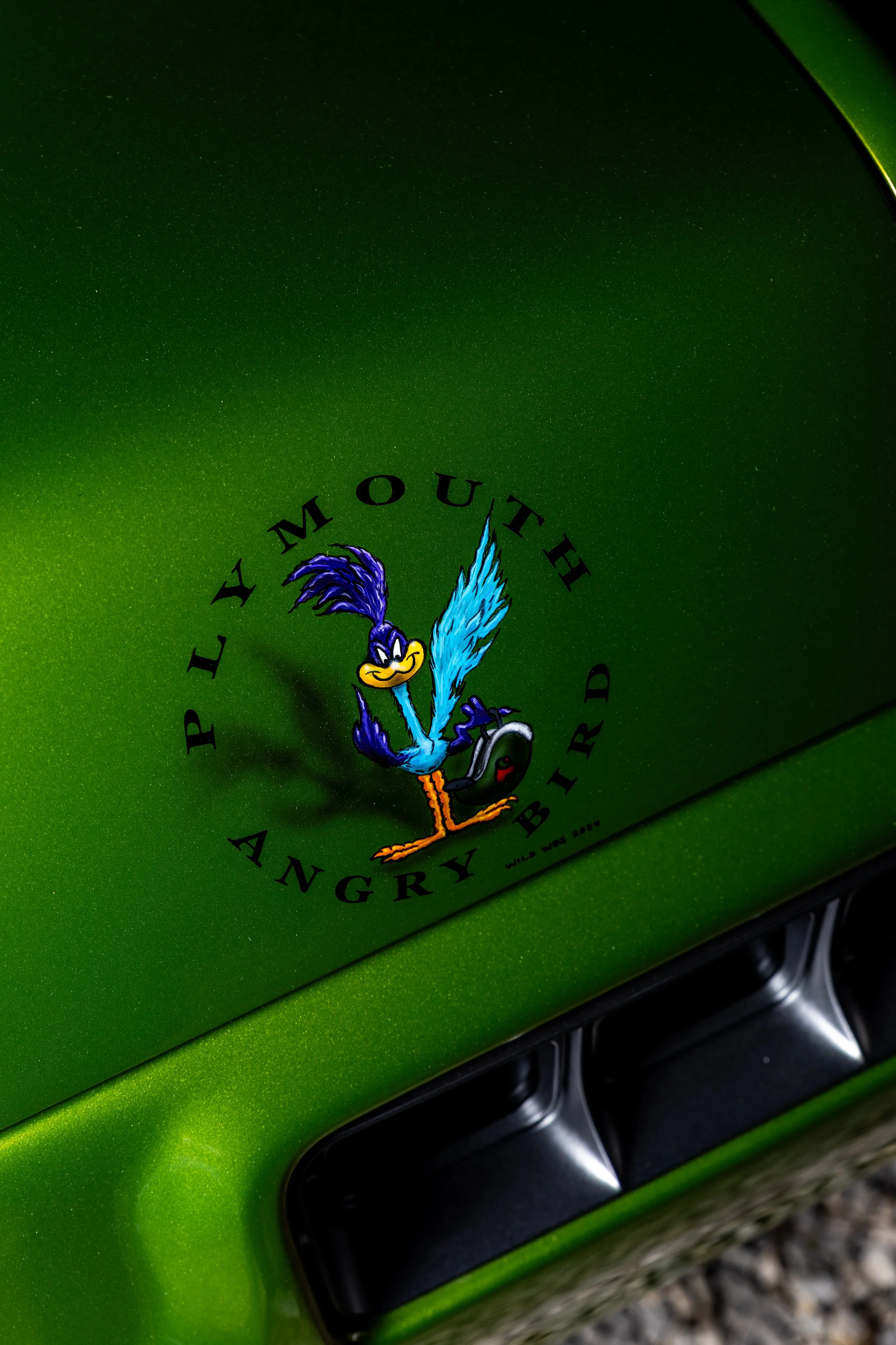 Green vehicle with a decal of a cartoon blue bird holding a black device, with the text "Plymouth Angry Mouthed" around it.