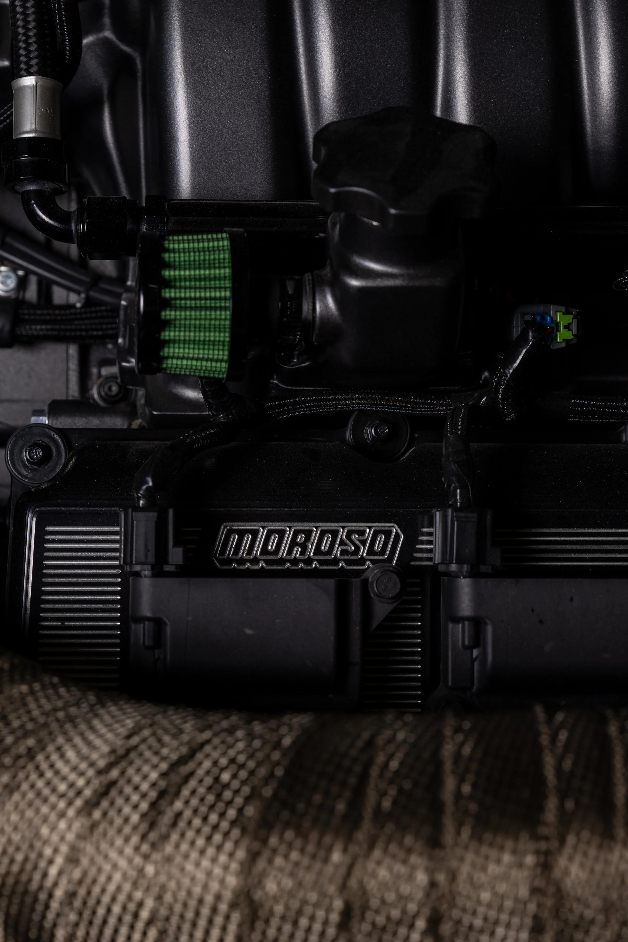 Close-up of a Moroso engine component with a green air filter attached, mounted on a dark engine bay surface.