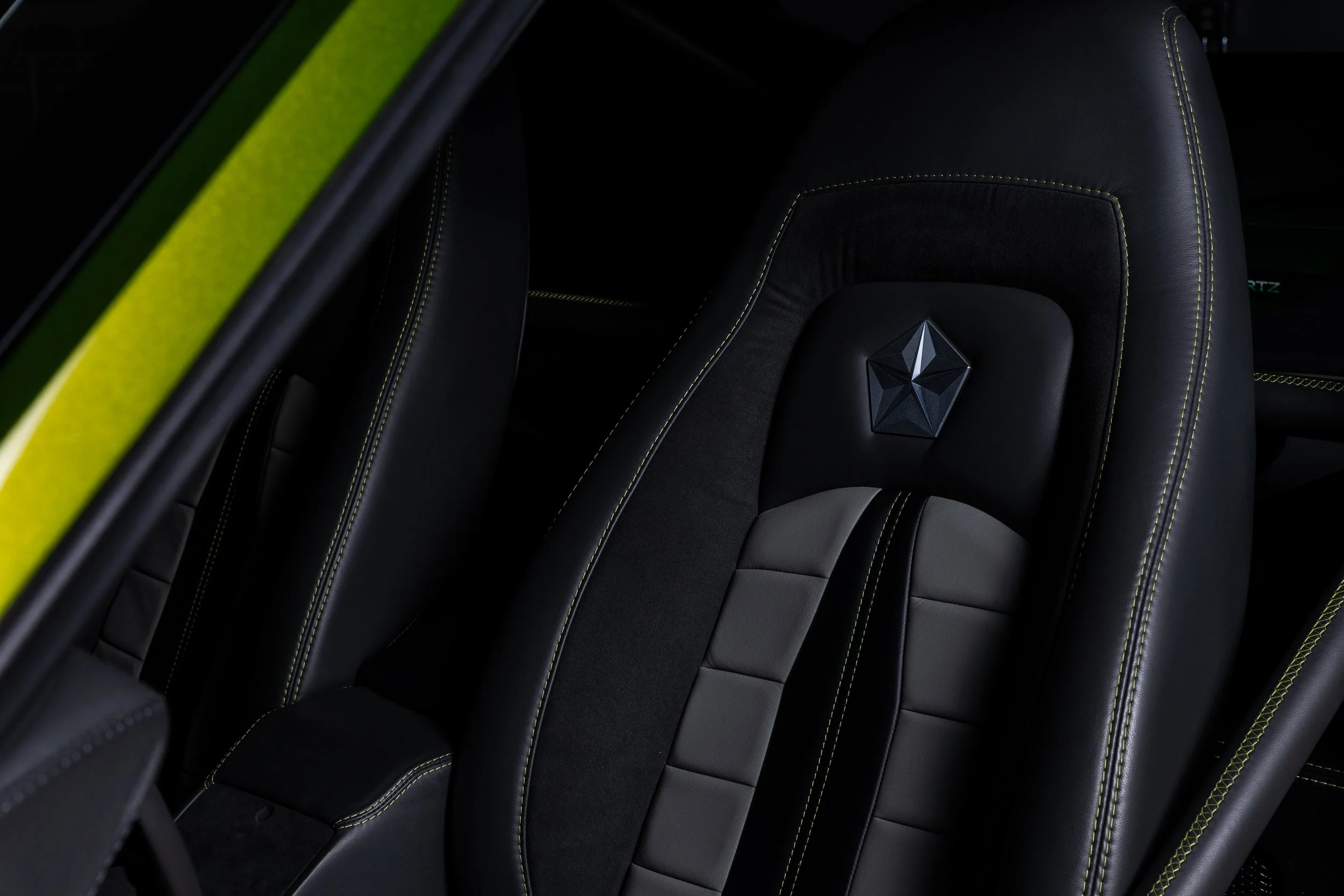 Close-up of a luxury black car seat with yellow stitching and a diamond-shaped emblem on the headrest.